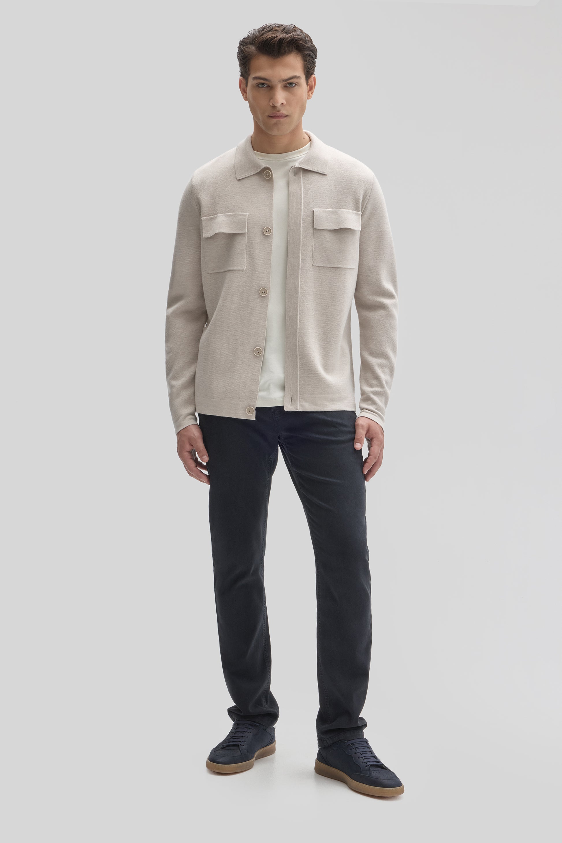 Beige buttoned cardigan with chest pockets worn over white undershirt and dark navy pants.