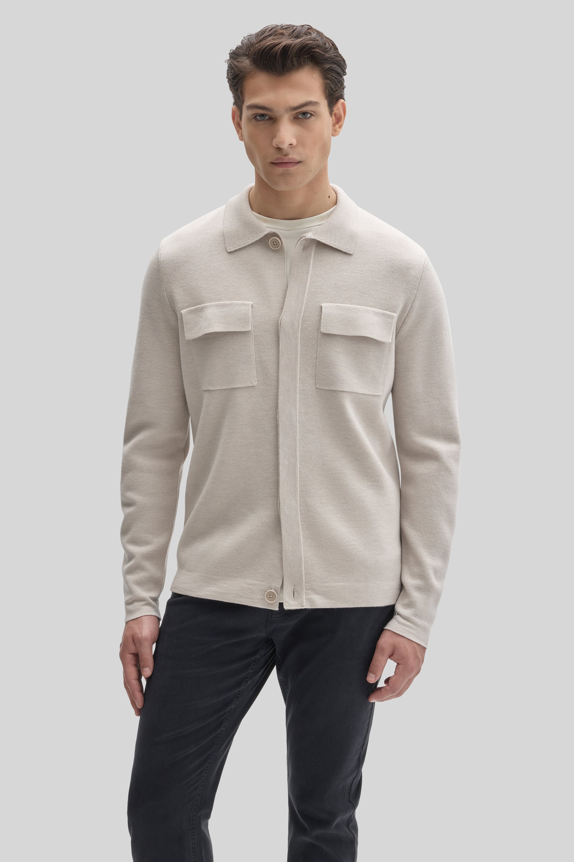 Cream buttoned cardigan with collared neckline and front chest pockets worn over black trousers.