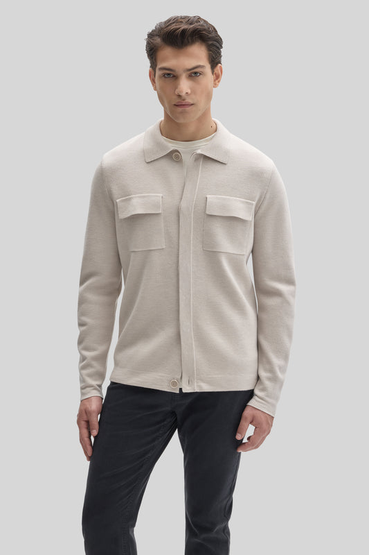 Cream buttoned cardigan with collared neckline and front chest pockets worn over black trousers.