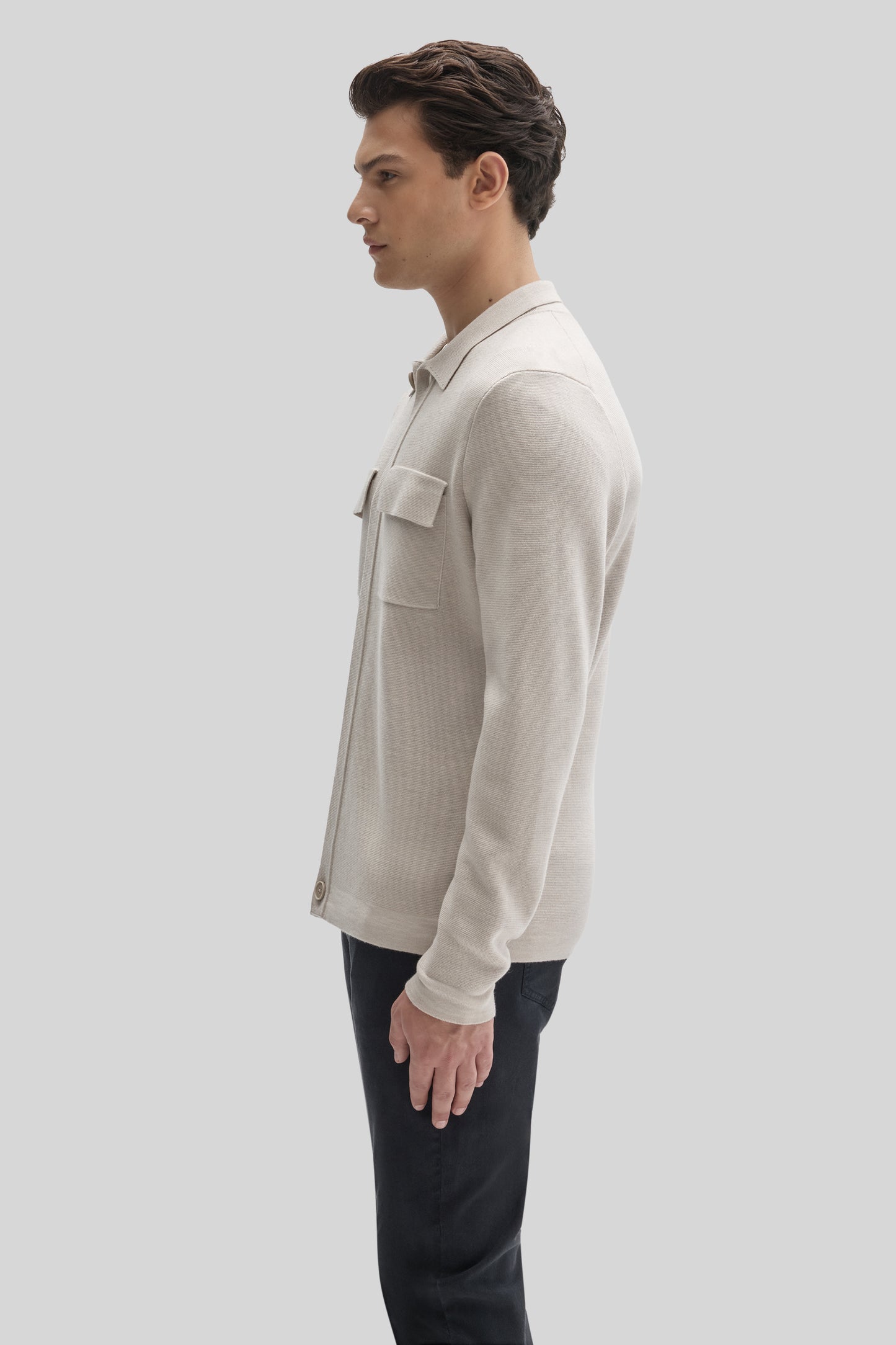 Cream-colored buttoned cardigan with chest pocket worn over black pants, shown from the side.