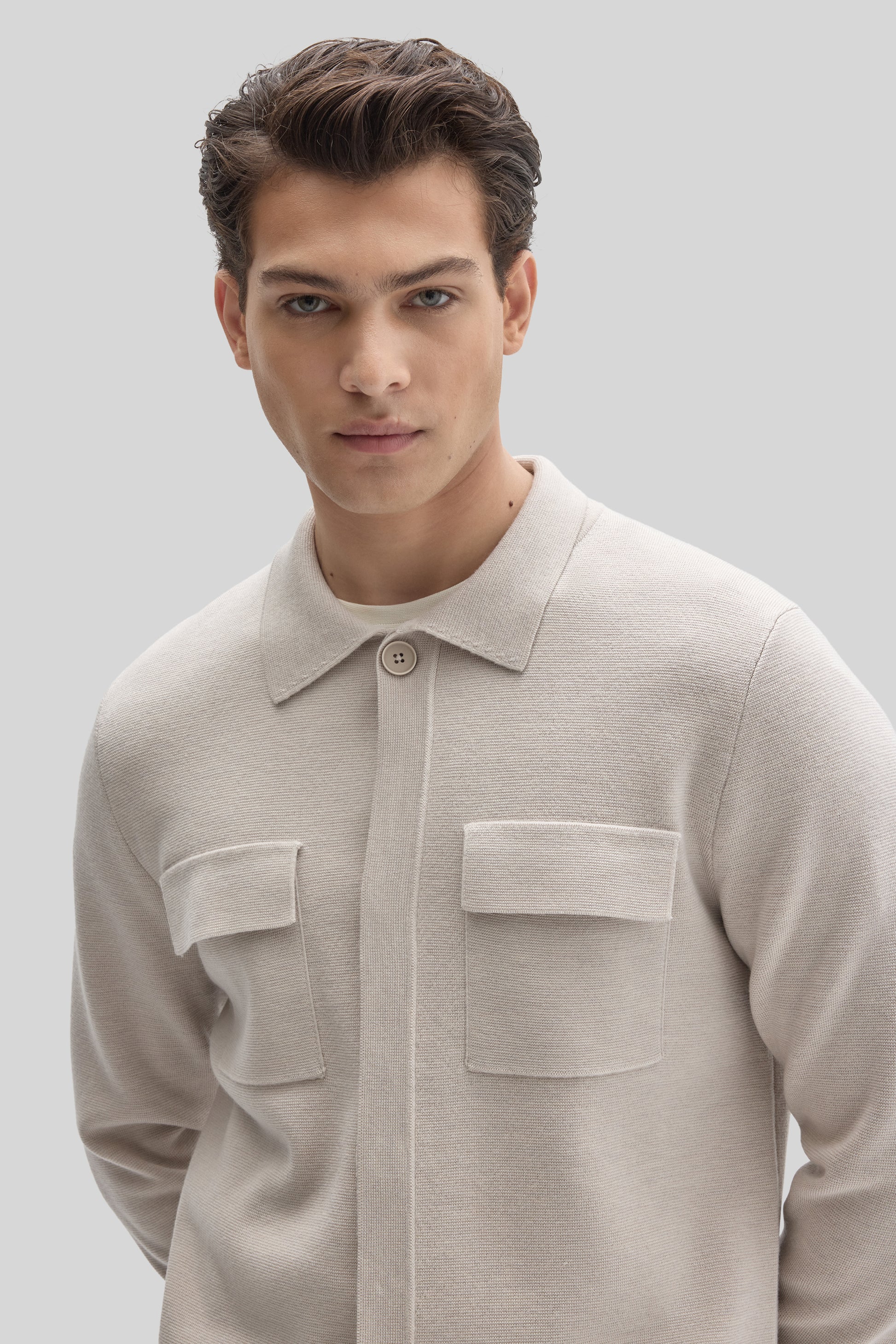 Beige buttoned cardigan with collar and chest pockets worn by a man against a neutral background.