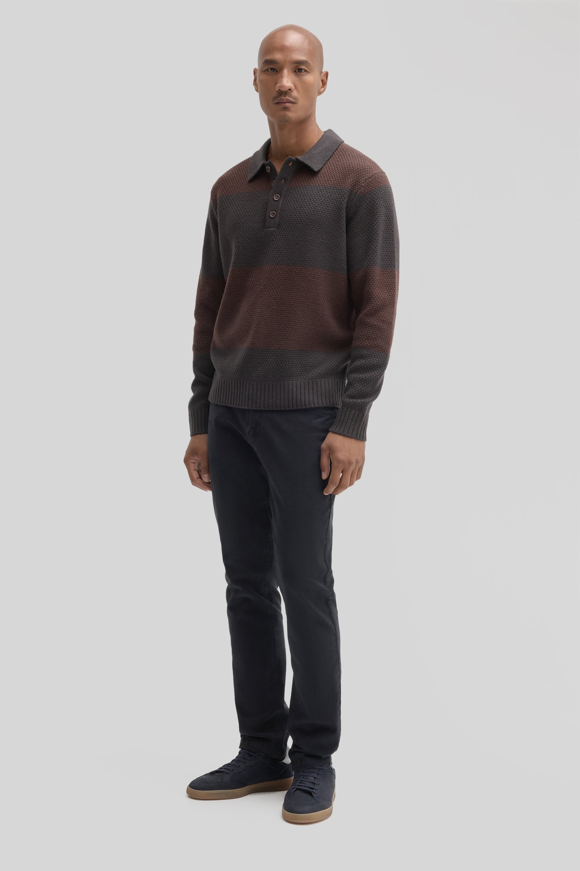 Man wearing charcoal and burgundy striped rugby polo sweater with collar and buttons, paired with dark jeans.