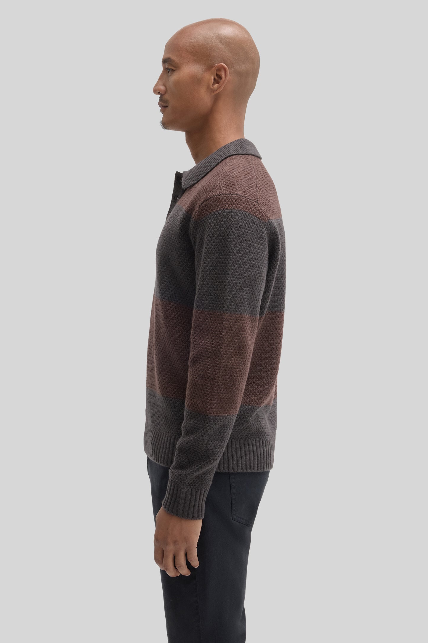 Man wearing brown and charcoal colorblock rugby polo sweater with ribbed collar and cuffs, paired with black pants.