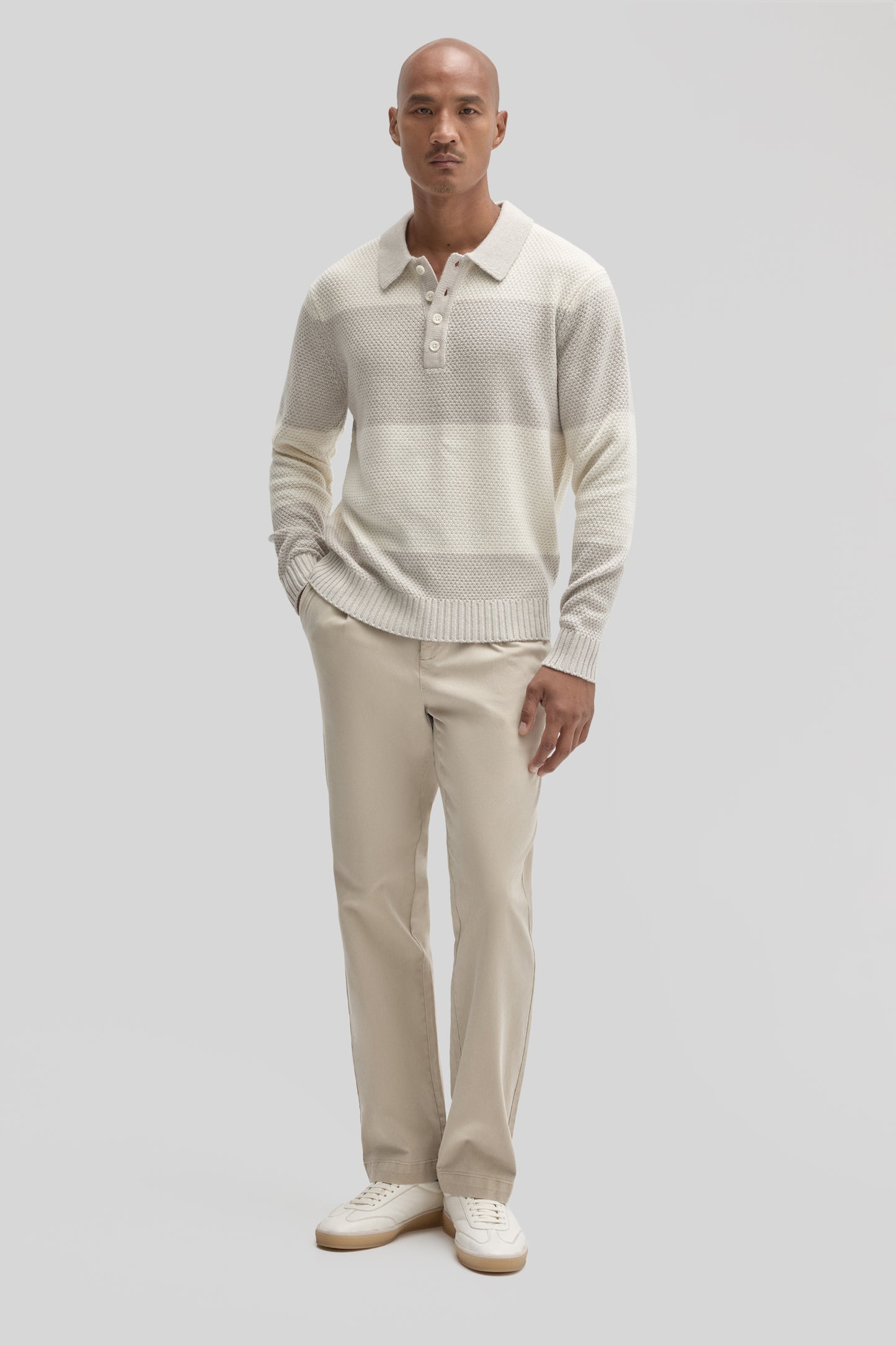 Cream textured rugby polo sweater with button placket, worn with beige trousers and white sneakers.