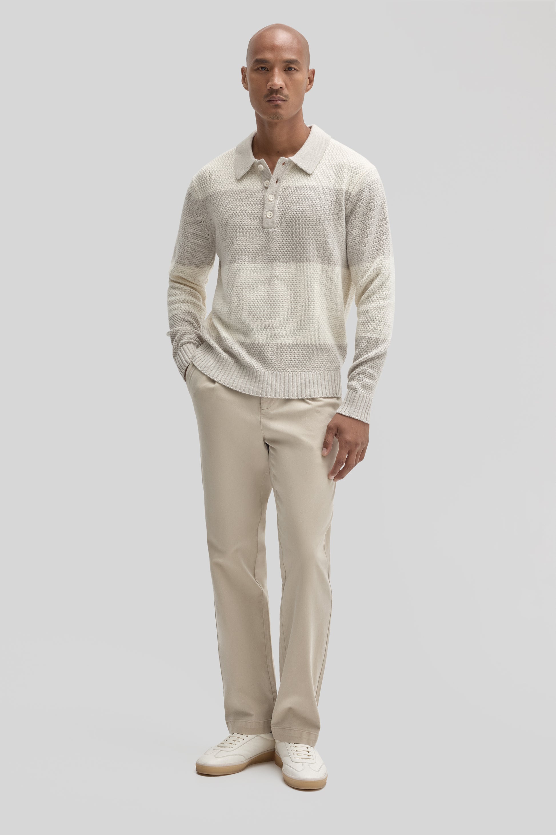 Cream textured rugby polo sweater with button placket, worn with beige trousers and white sneakers.