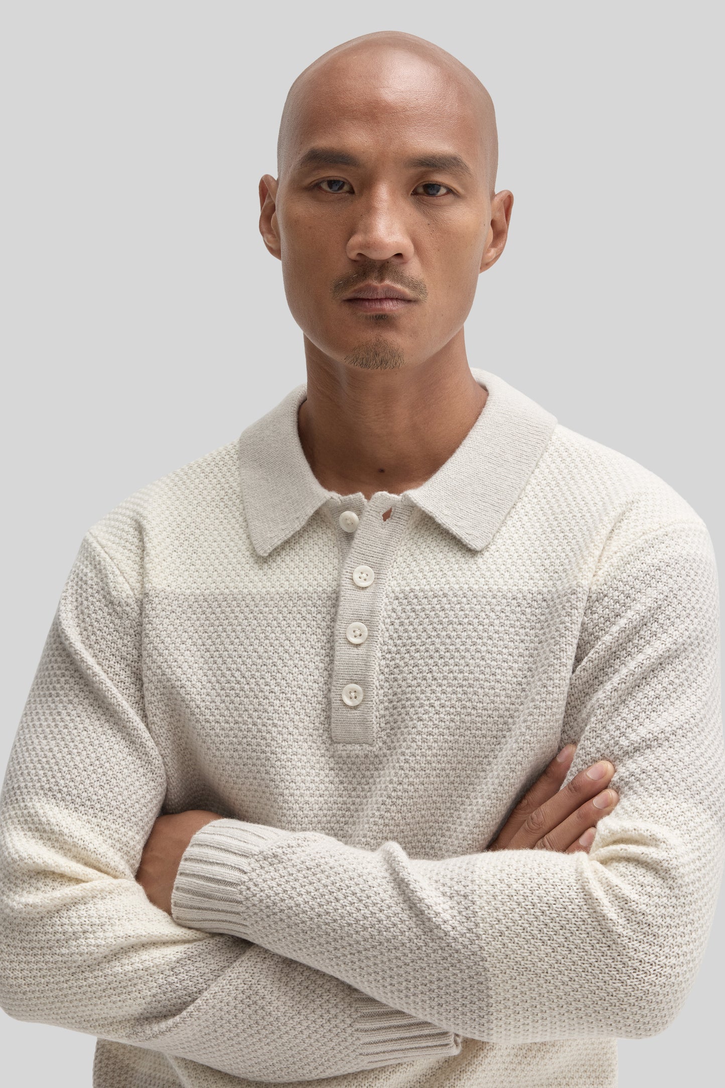 Cream-colored rugby polo sweater with textured knit fabric, collar, and button placket worn by man against neutral background