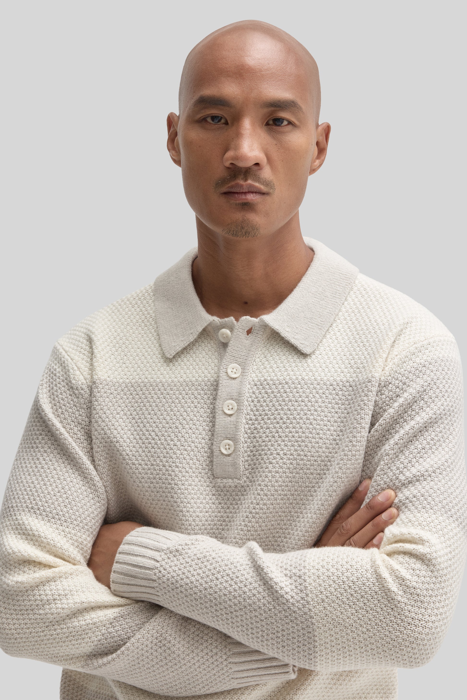 Cream-colored rugby polo sweater with textured knit fabric, collar, and button placket worn by man against neutral background