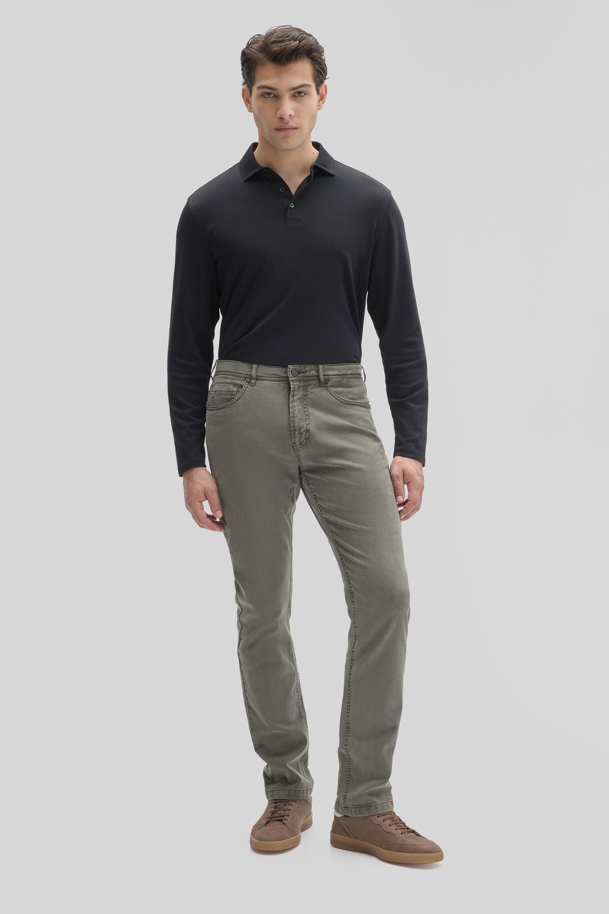 Man wearing gray five-pocket stretch pants with black polo shirt and brown shoes.