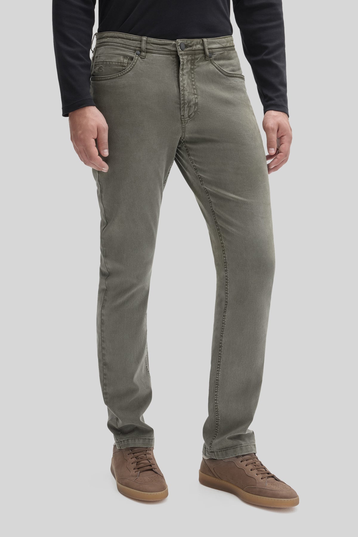 Khaki five-pocket stretch pants with button fly on model wearing black long-sleeve shirt and brown lace-up boots.