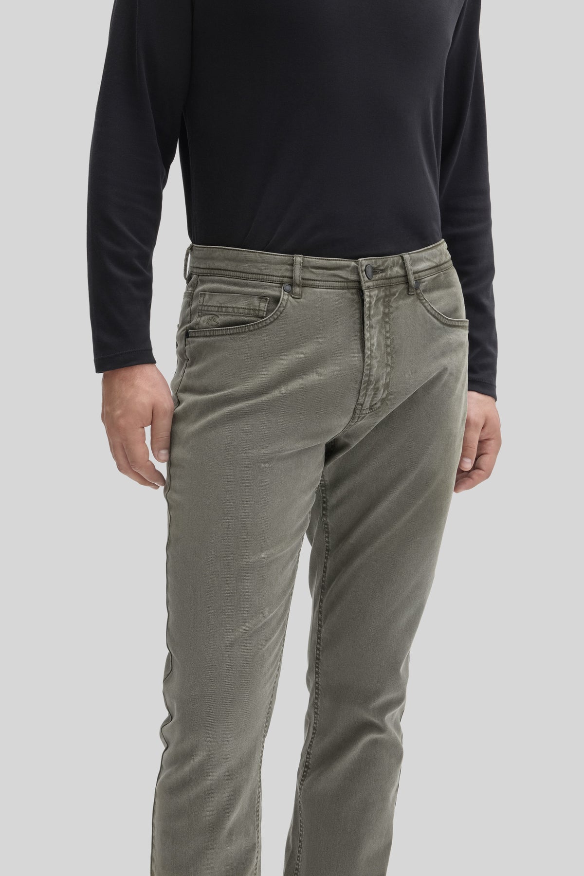 Sage-green five-pocket pants with zip fly and belt loops, worn with black long-sleeve shirt.