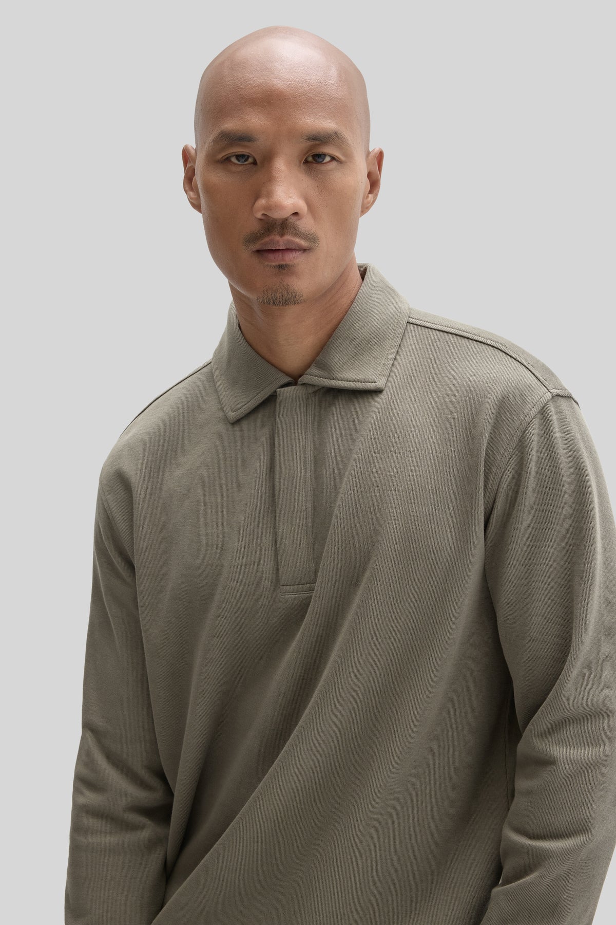 Man wearing a beige long-sleeve polo shirt with a snap front closure and ribbed collar.