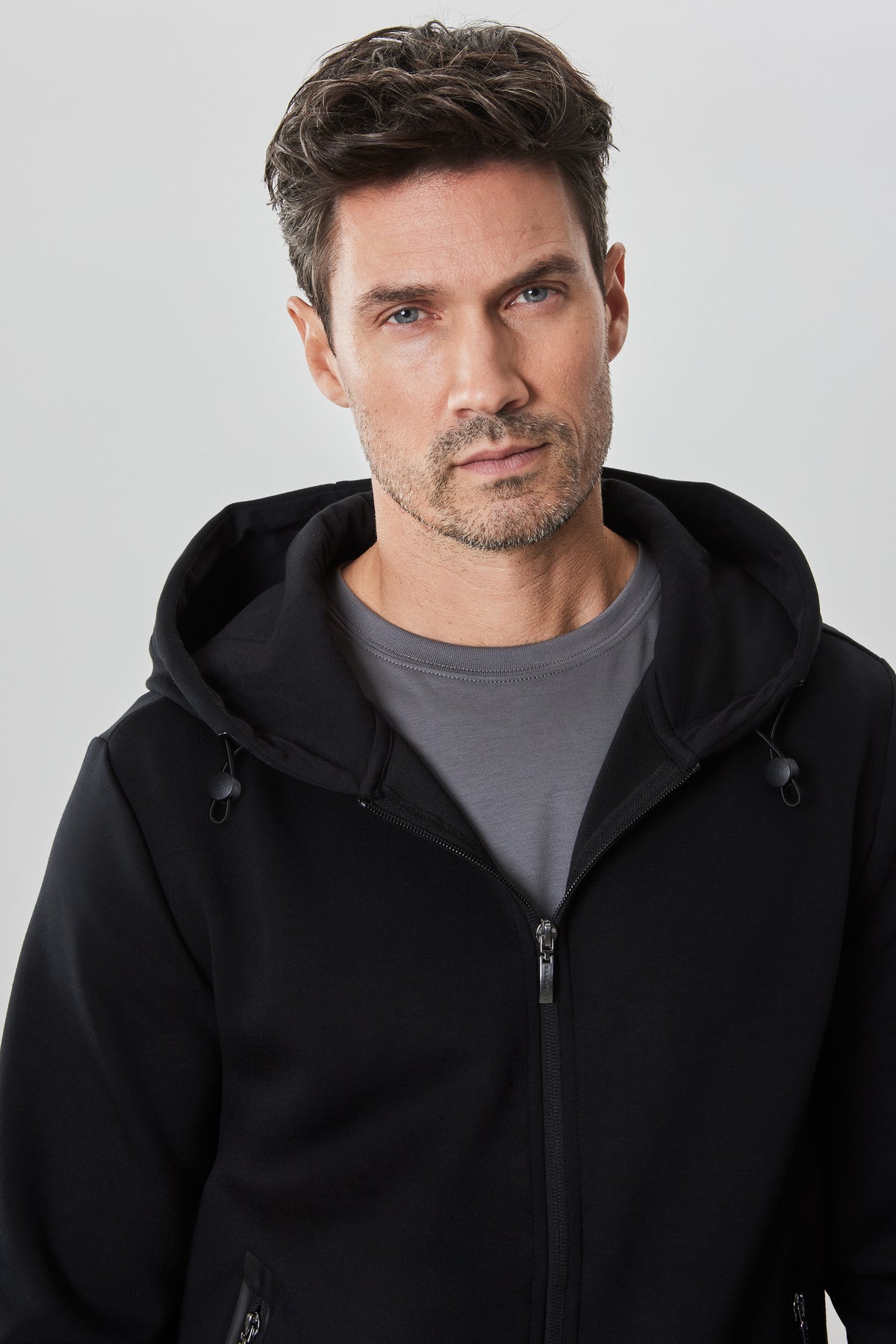 Man wearing black zip hoodie with gray t-shirt underneath and drawstring hood.