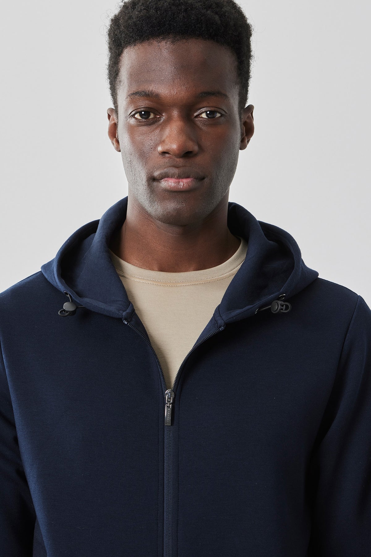 Navy zip-up hoodie with drawstring hood and front zipper, worn over a beige t-shirt.