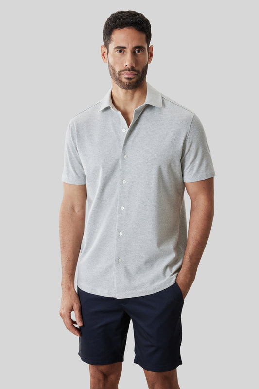Light gray short-sleeve knit shirt with white buttons and collar, worn with navy shorts.