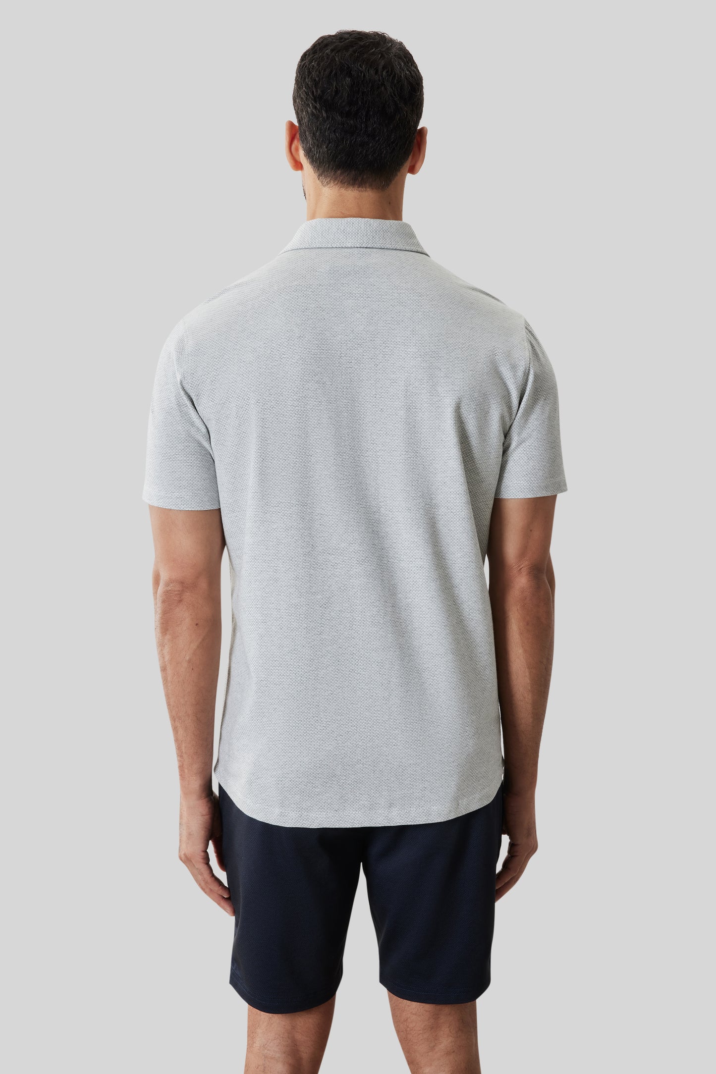 Man wearing light gray short-sleeve collared knit shirt with dark navy shorts, shown from back.