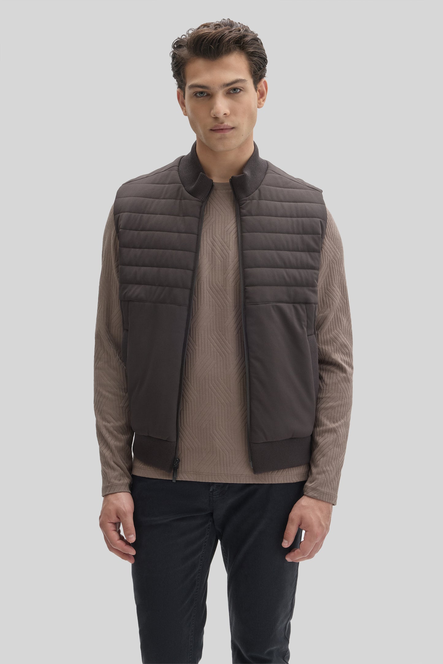 Man wearing charcoal quilted vest with ribbed collar over taupe long-sleeve shirt and navy pants.