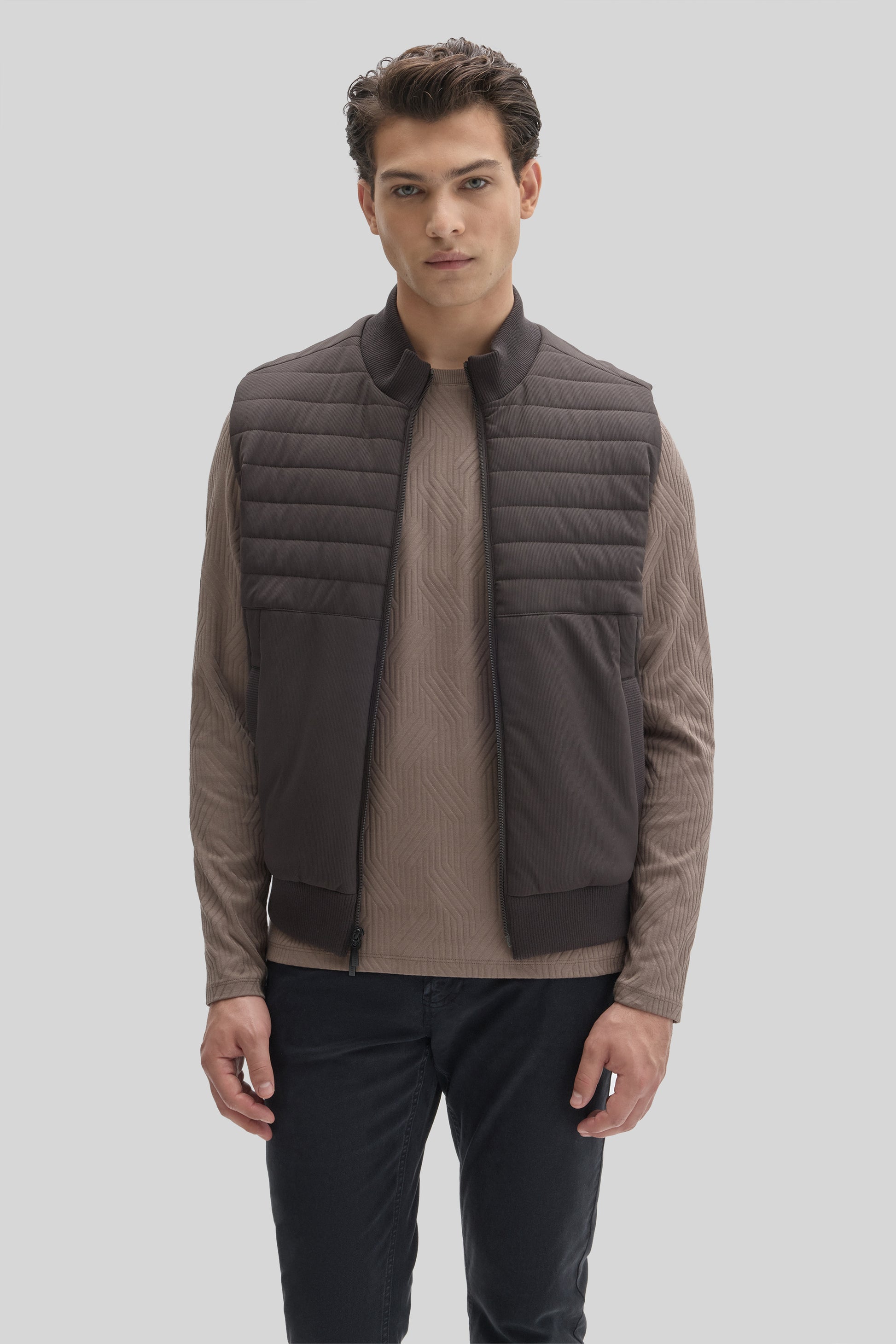 Man wearing charcoal quilted vest with ribbed collar over taupe long-sleeve shirt and navy pants.