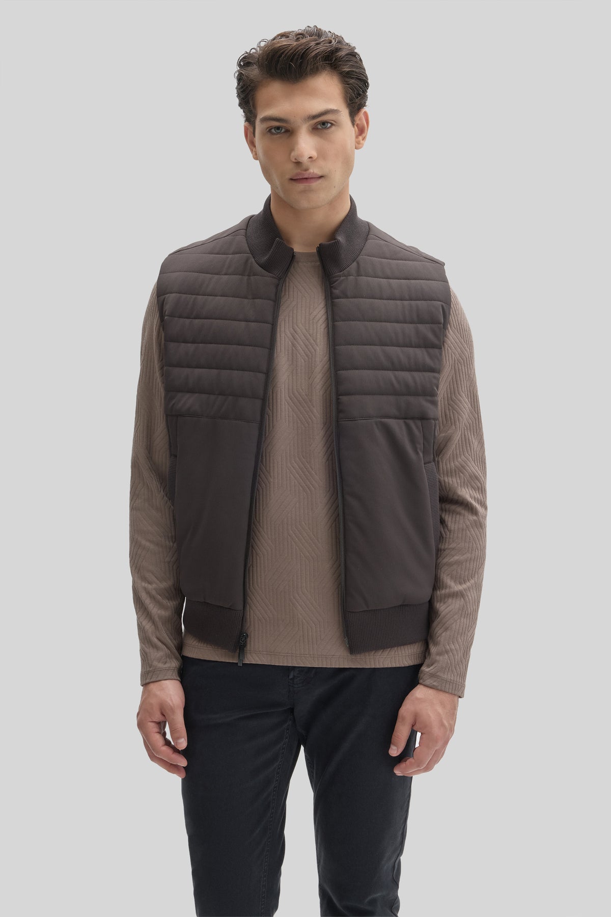 Man wearing charcoal quilted vest with ribbed collar over taupe long-sleeve shirt and navy pants.