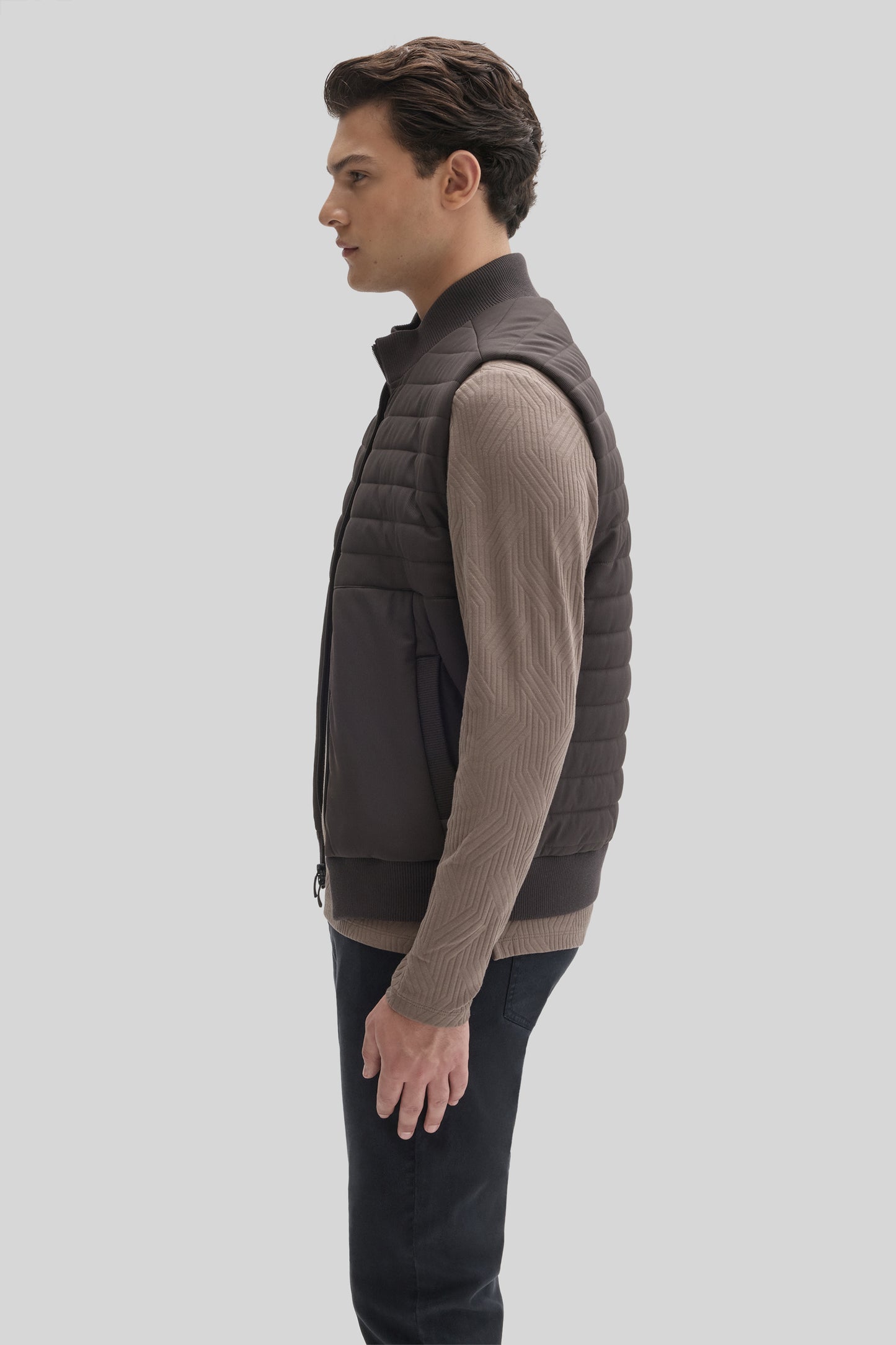 Man wearing charcoal quilted vest with ribbed knit sleeves and mock neck, paired with black pants.