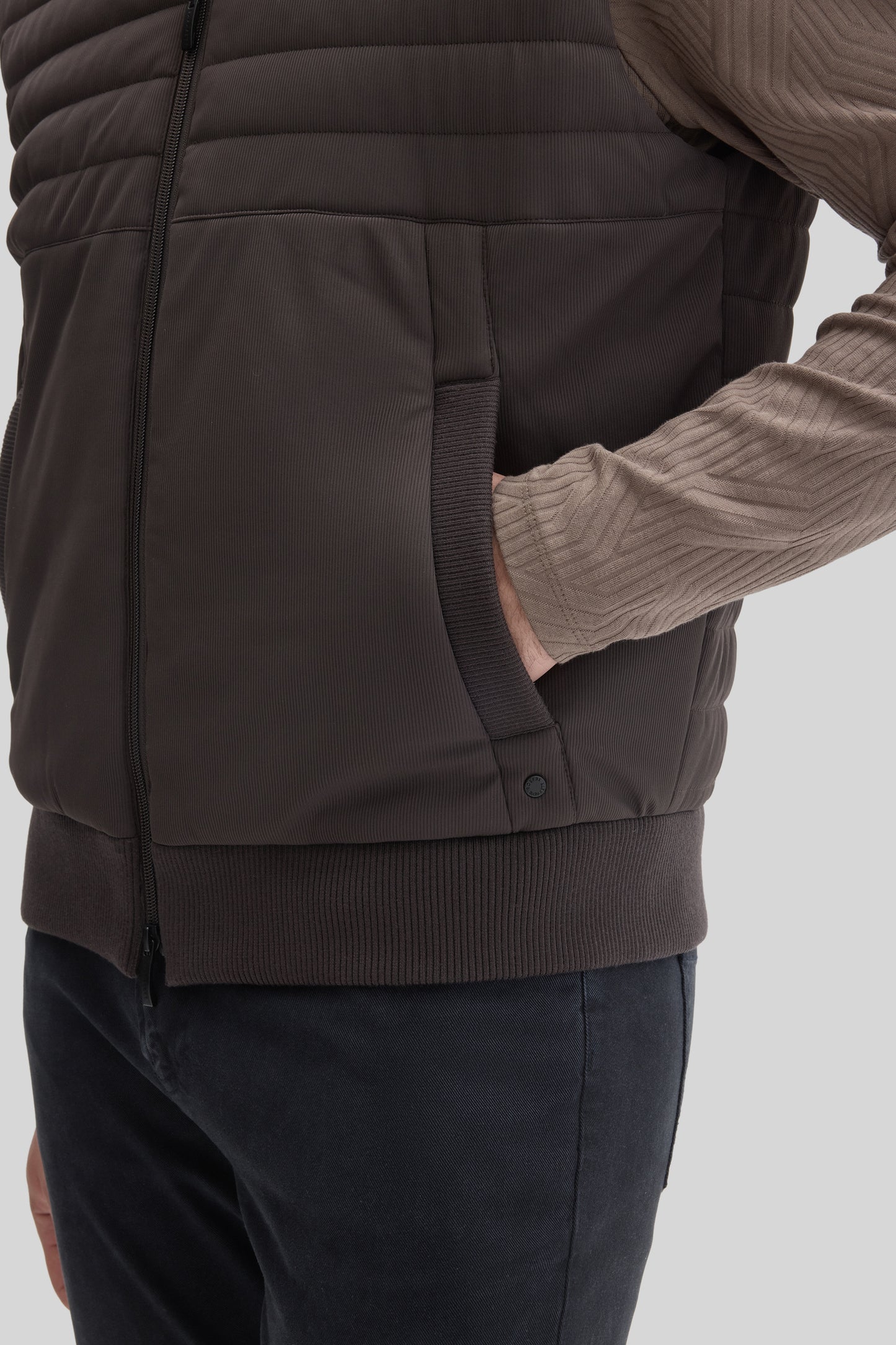Charcoal quilted vest with front zip closure and ribbed trim, worn over a tan ribbed long-sleeve shirt.