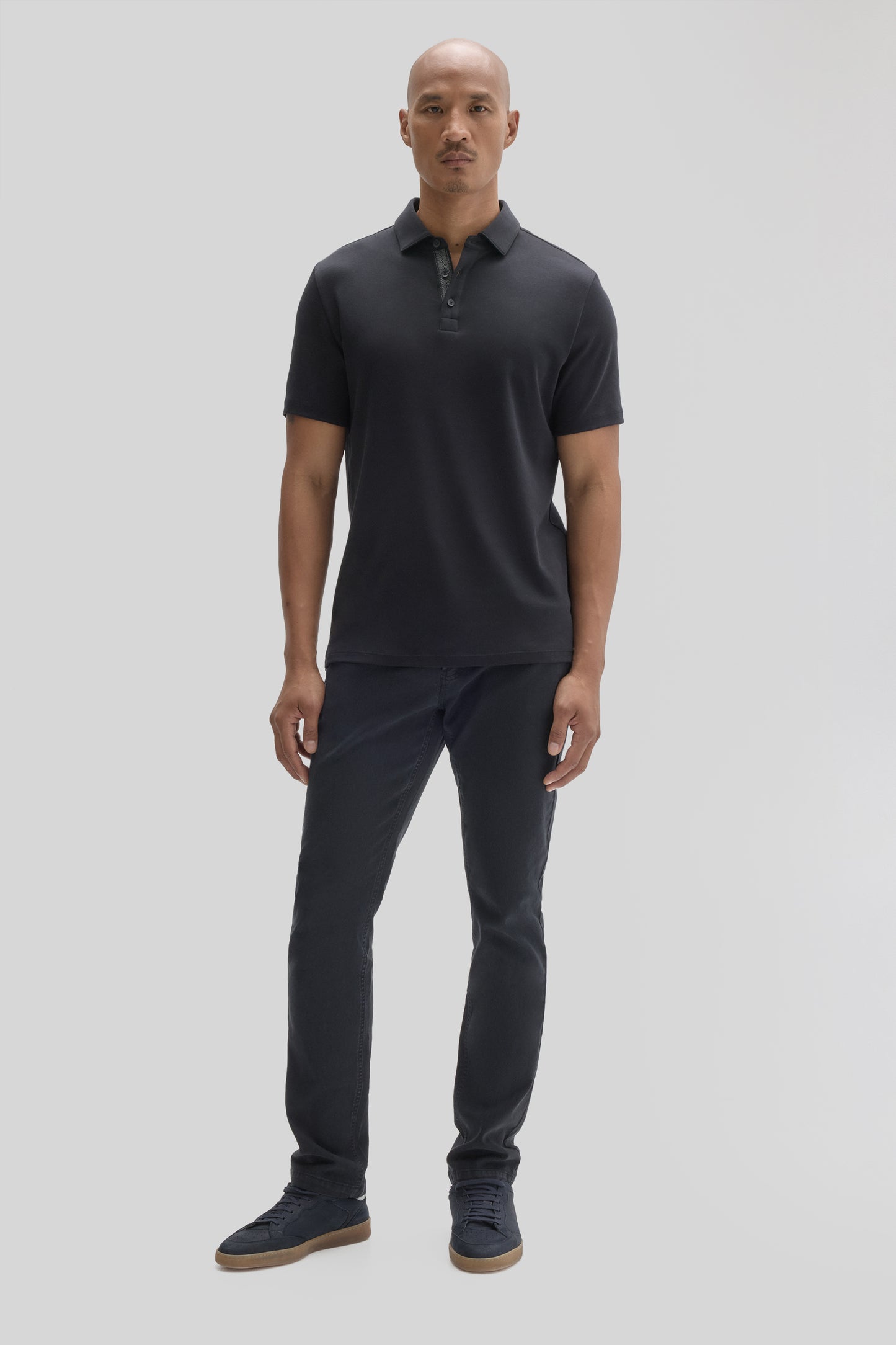 Man wearing dark navy short-sleeve polo shirt with collar and button placket, paired with dark jeans and navy sneakers.
