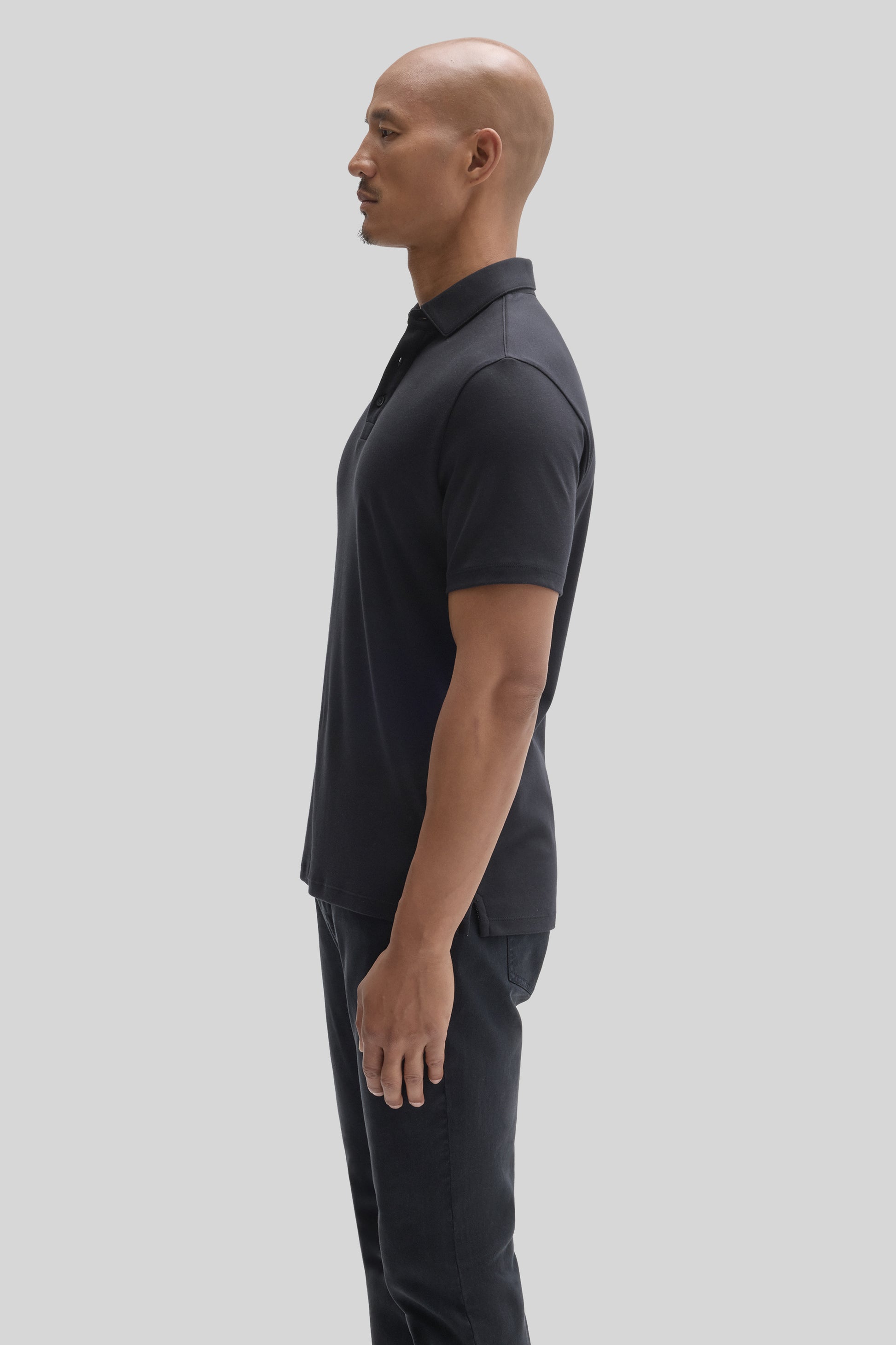 Man wearing dark charcoal short-sleeve polo shirt with herringbone texture and matching trousers, shown in profile.