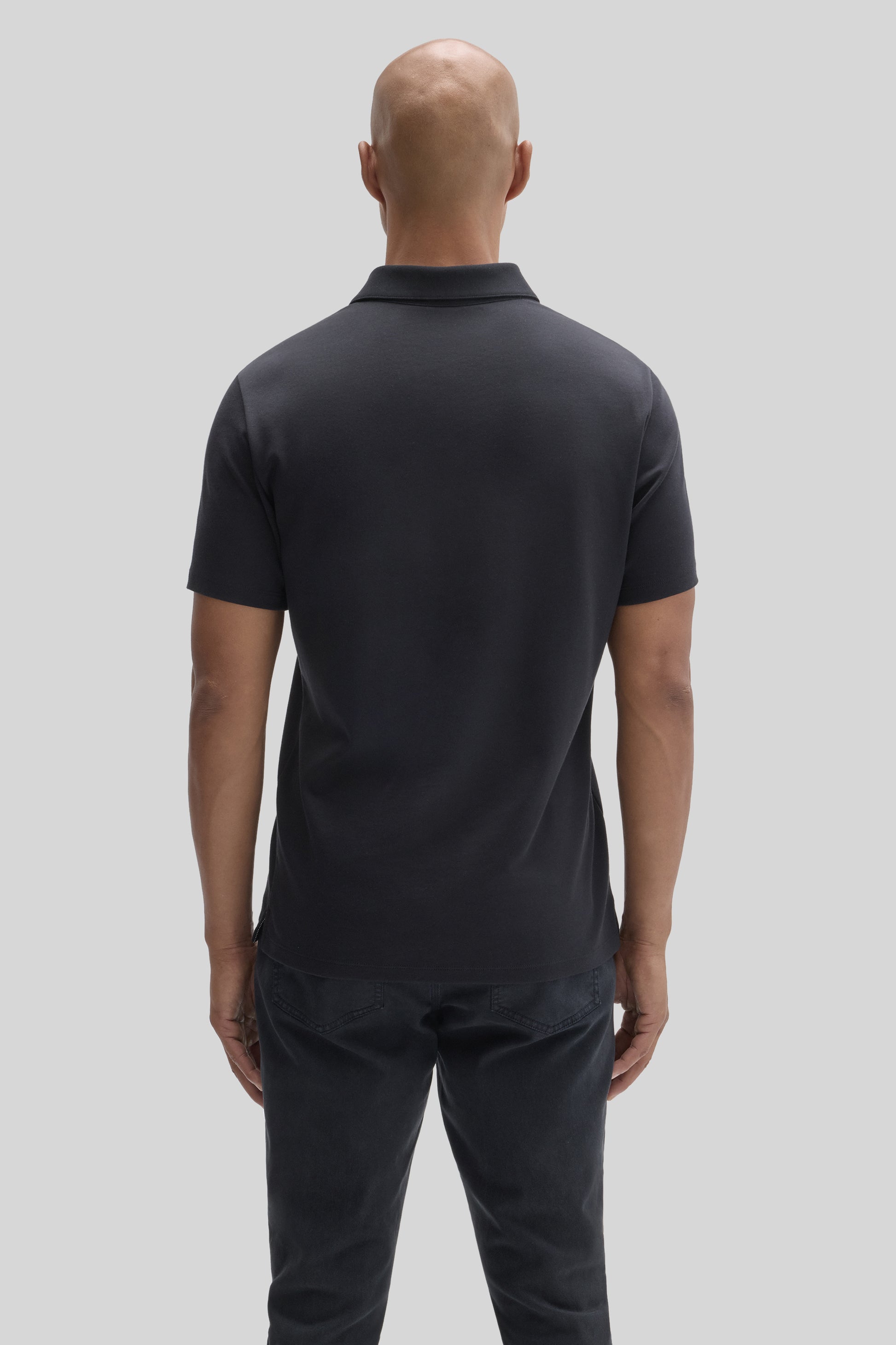 Man wearing black short-sleeve polo shirt with collar, shown from behind, paired with dark jeans.