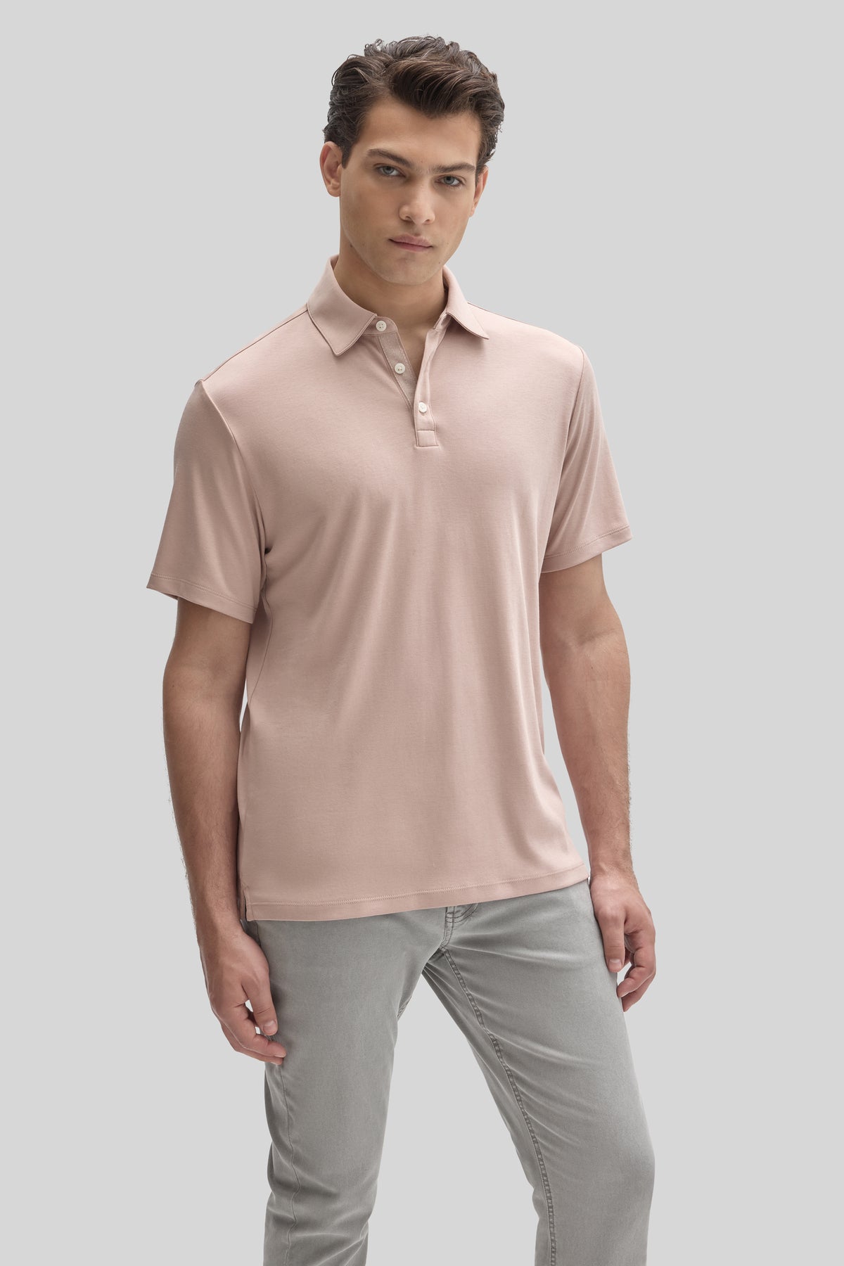 Man wearing light pink short-sleeve polo shirt with collar and button placket, paired with gray pants.