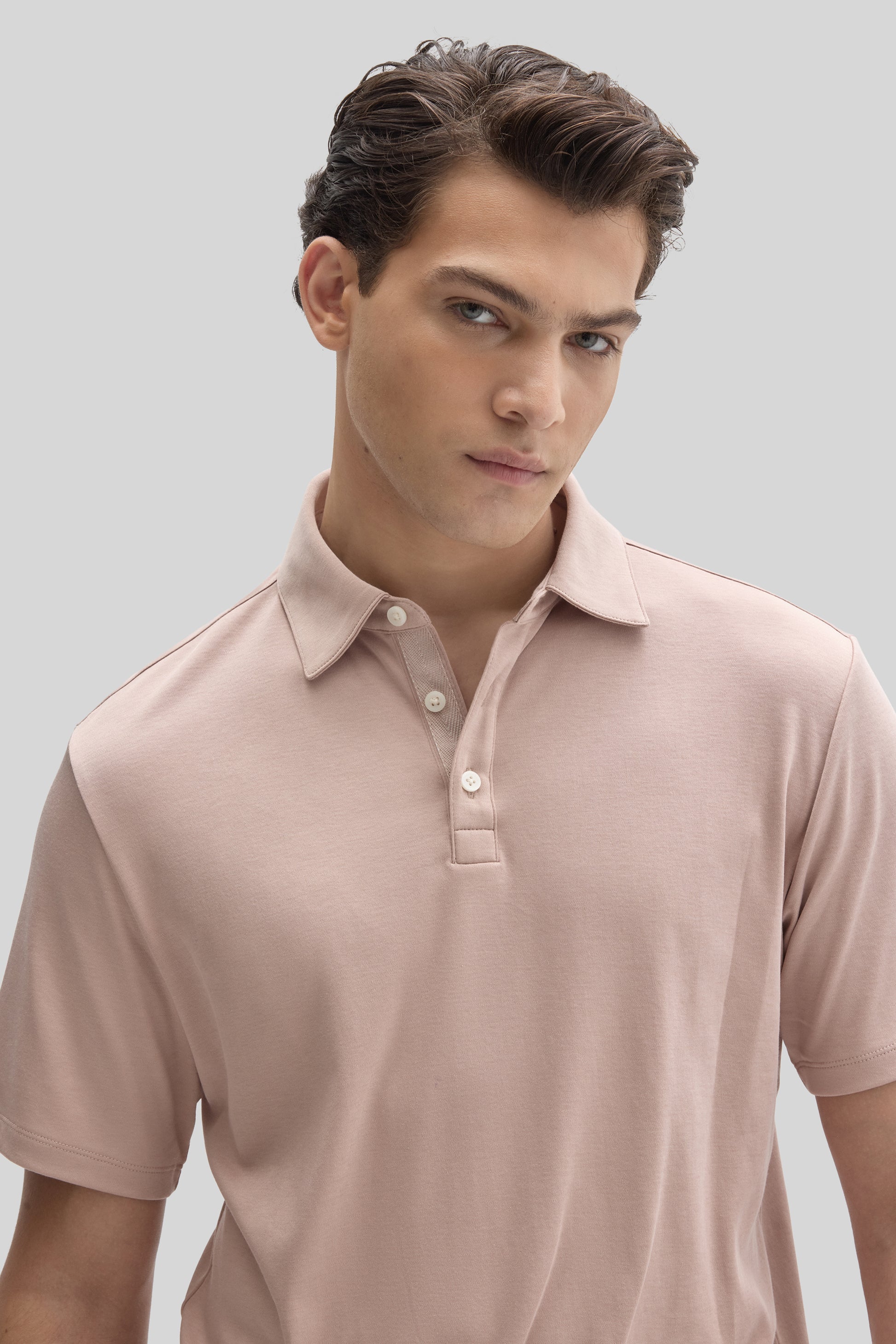 Man wearing a light pink herringbone polo shirt with a collar and white buttons.