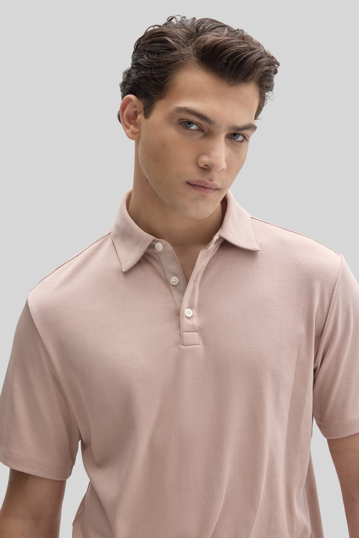 Man wearing a light pink herringbone polo shirt with a collar and white buttons.