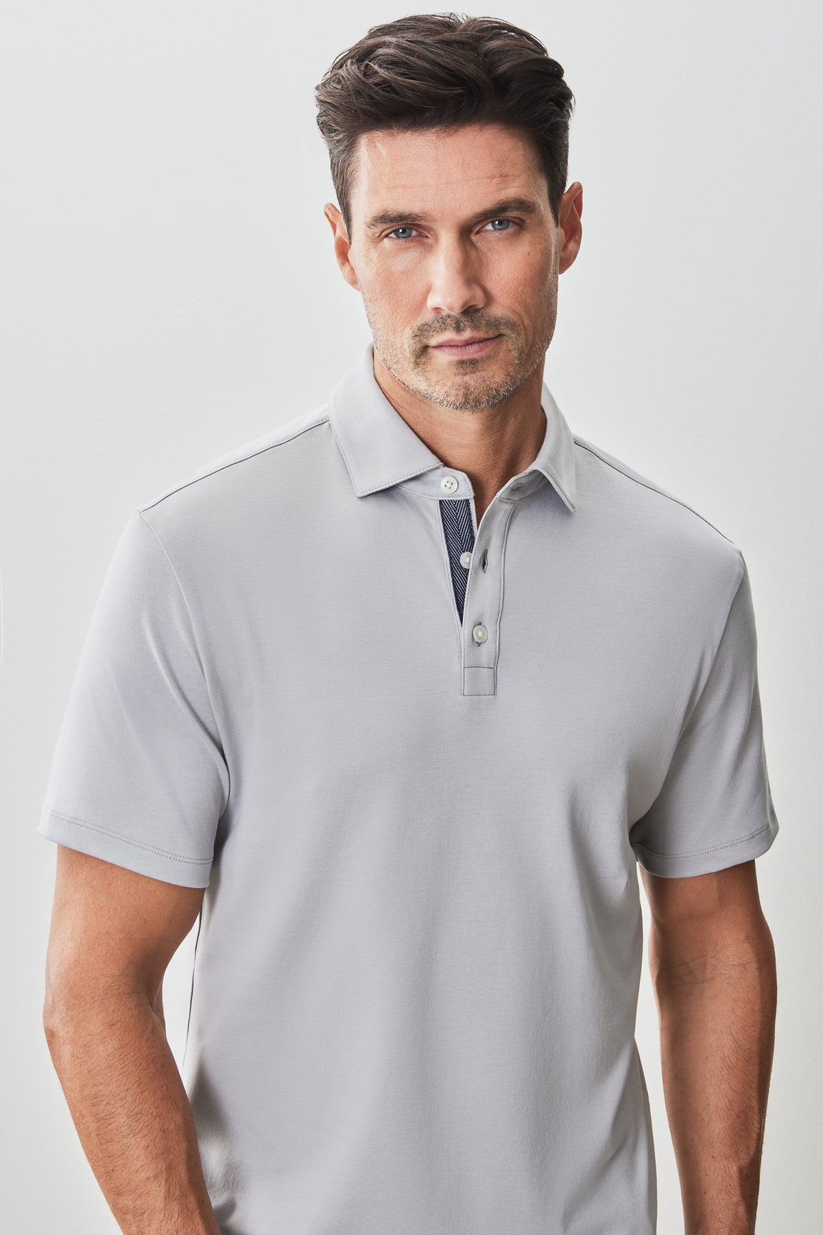 Man wearing light gray short-sleeve polo shirt with herringbone pattern interior placket and button closure.