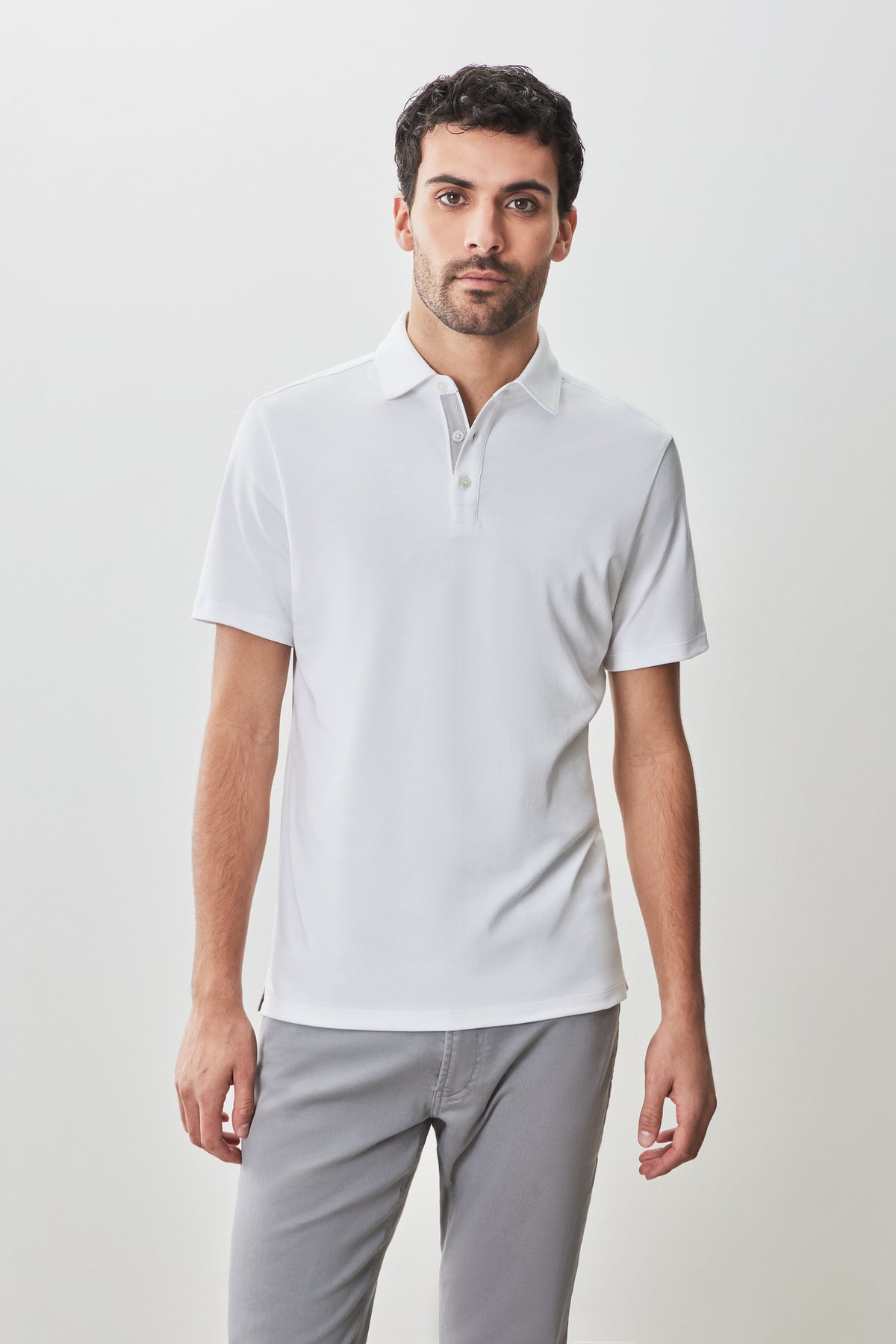 Man wearing white short-sleeve polo shirt with collar and button front, paired with gray pants.