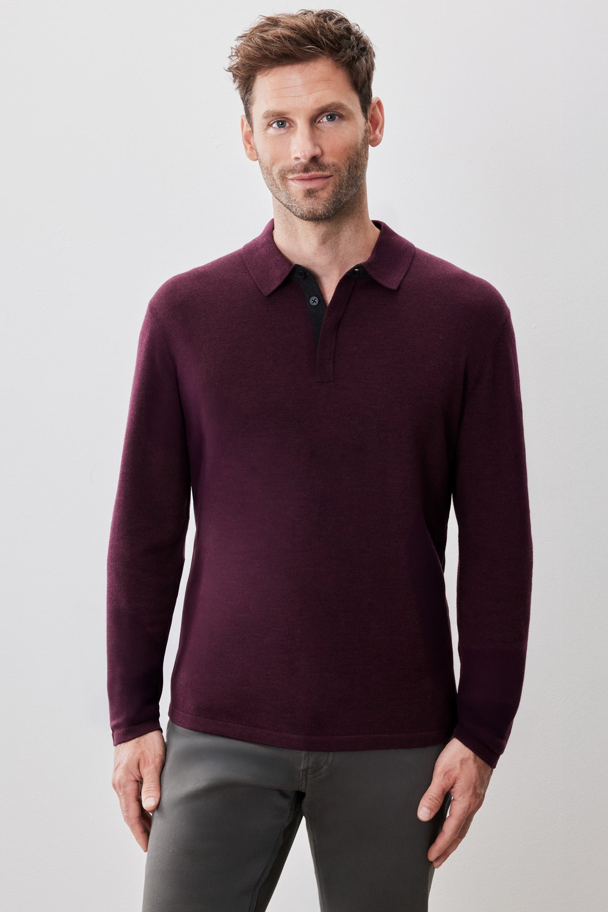 Man wearing burgundy long sleeve sweater polo with collar and dark button placket, paired with gray trousers.
