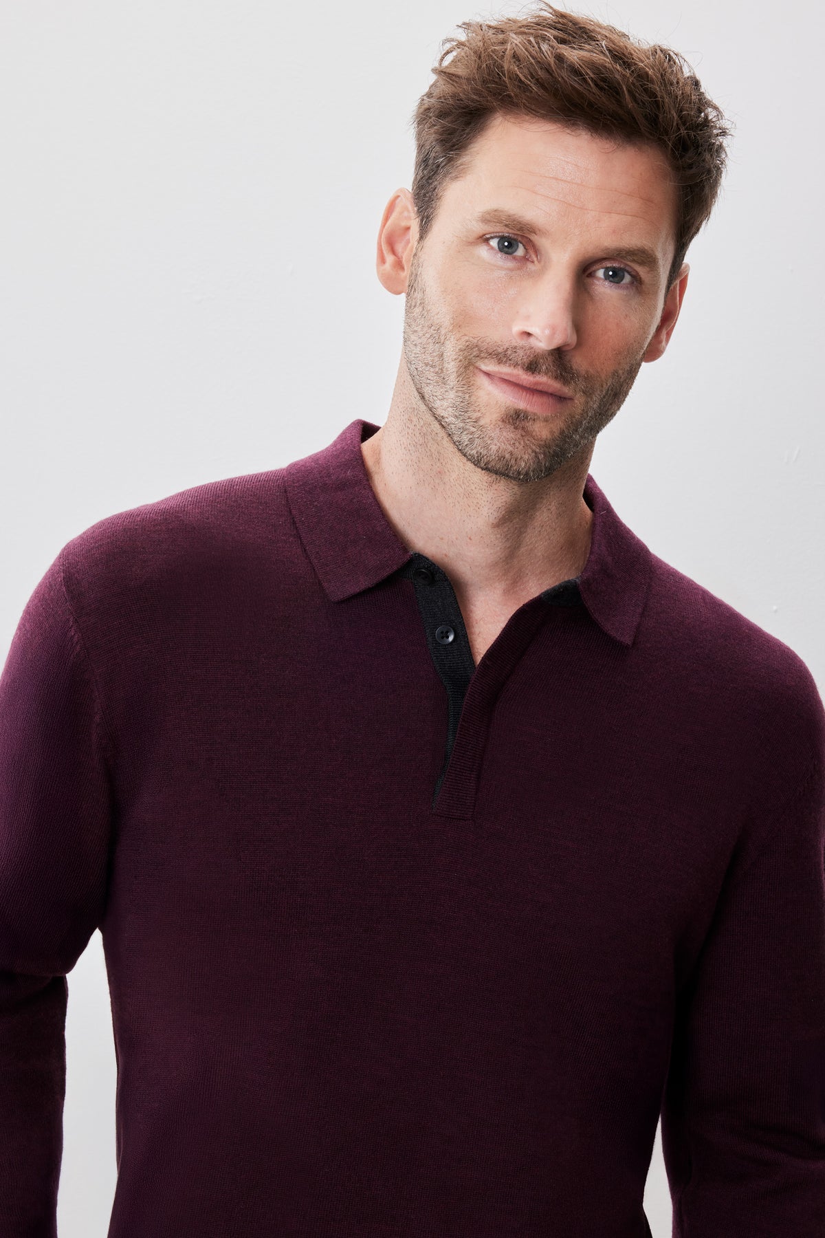 Man wearing burgundy long sleeve sweater polo with dark button placket and collar.