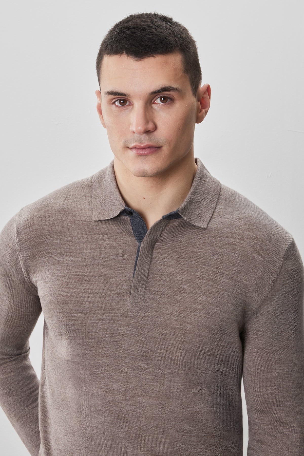 Man wearing a beige long sleeve polo sweater with a collar and button placket.