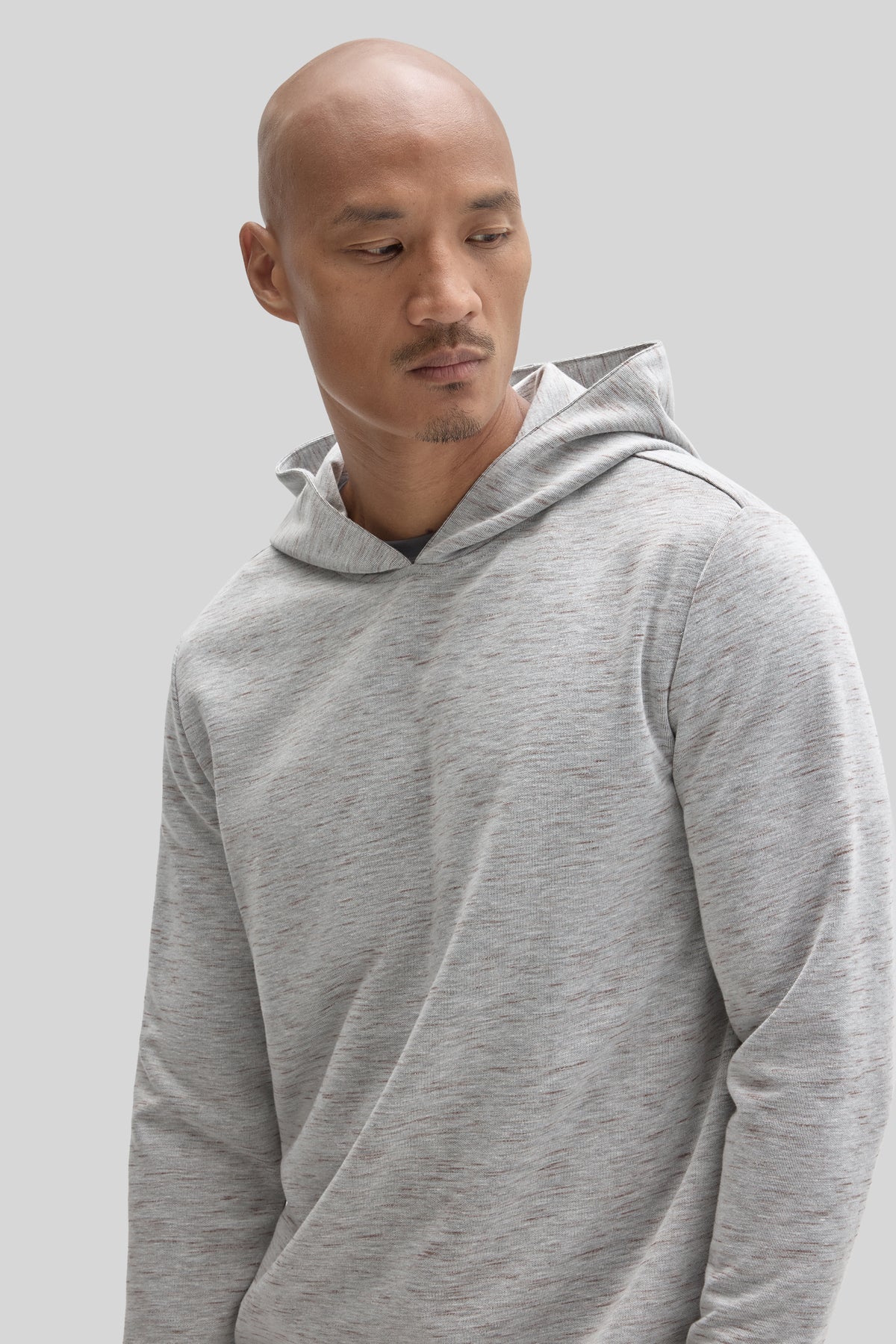 Man wearing a light gray heathered hoodie with a textured fabric and drawstring hood.