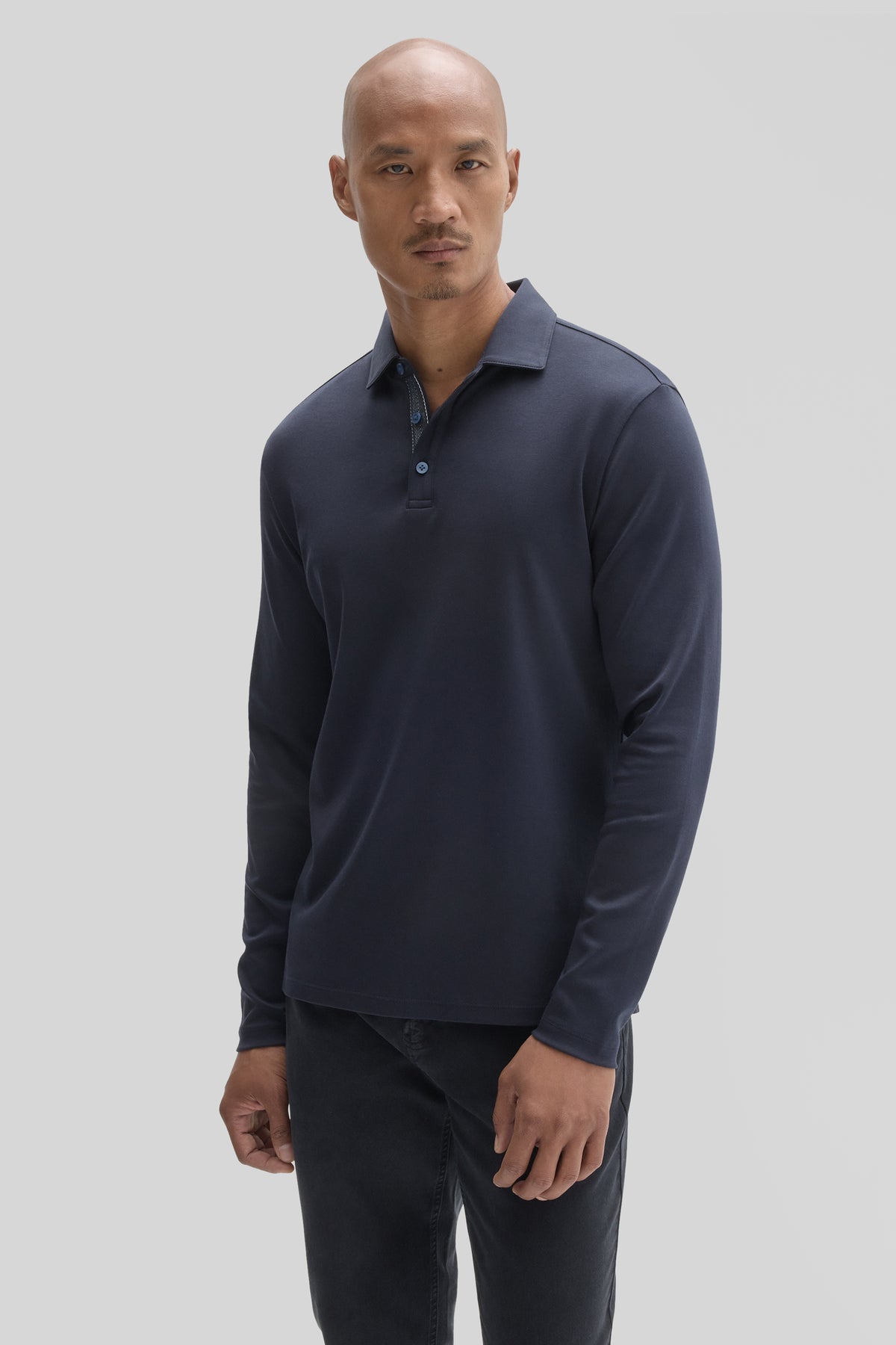 Man wearing navy long-sleeve polo with collar and button placket, paired with dark jeans.