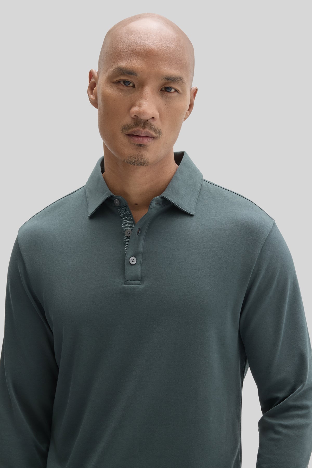 Man wearing sage green long-sleeve polo shirt with herringbone texture and button placket.