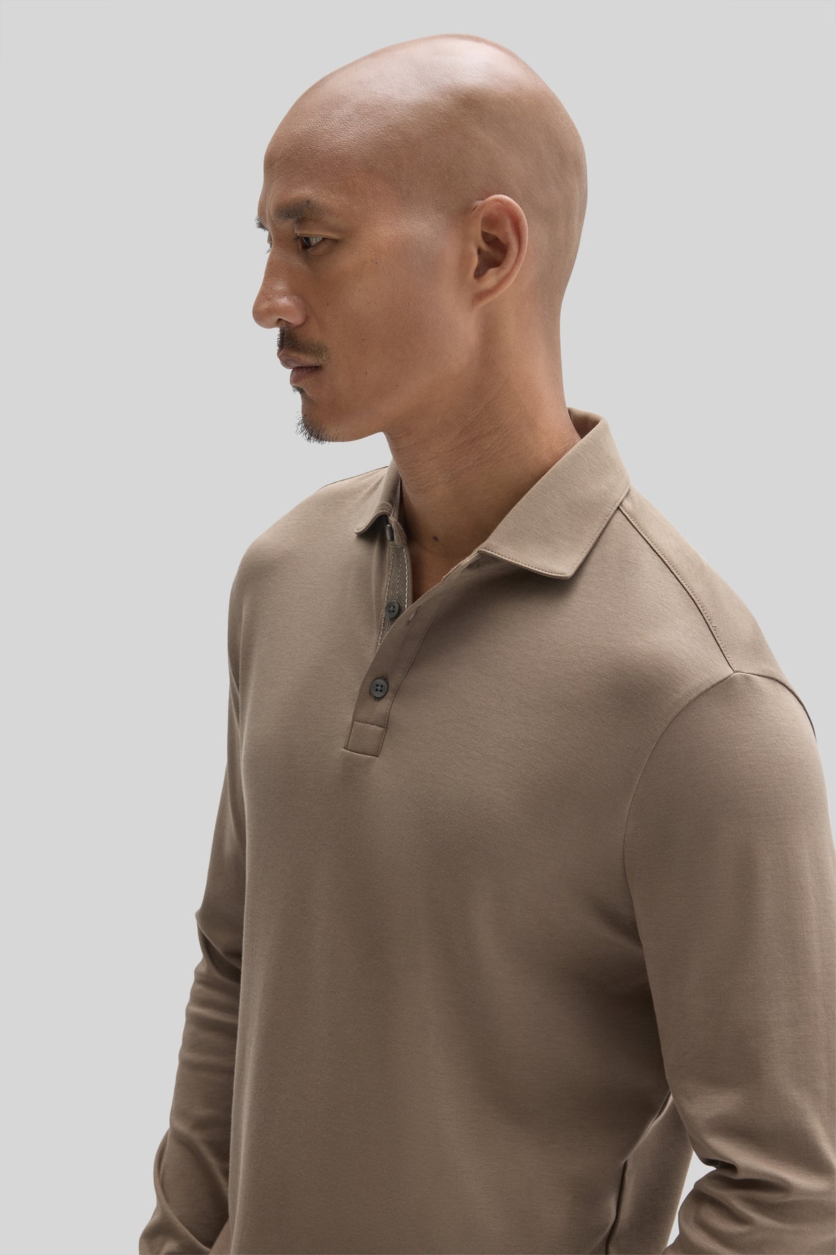 Beige long sleeve polo shirt with herringbone texture and collar, worn by man shown in profile.