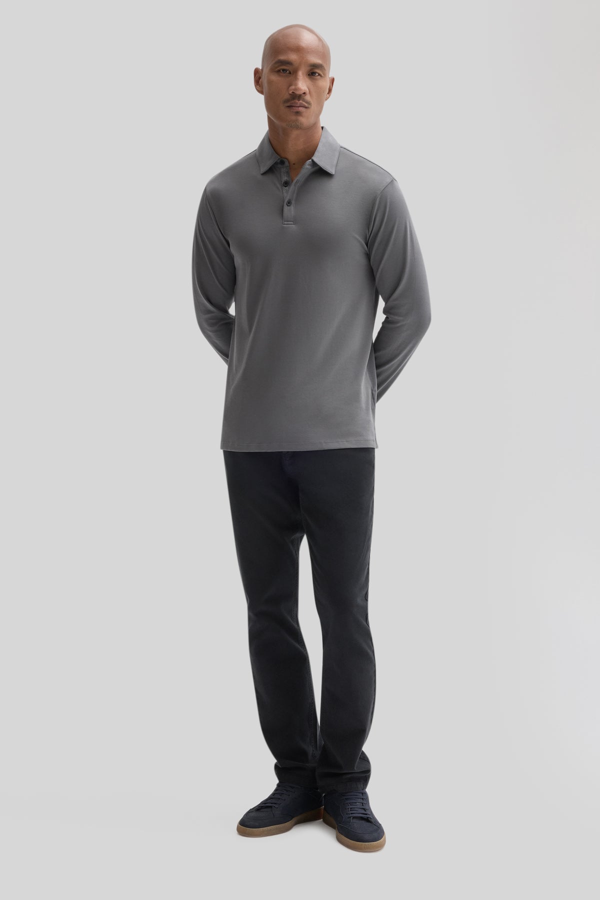 Man wearing gray long-sleeve herringbone polo shirt with collar and buttons, paired with black pants and navy sneakers.
