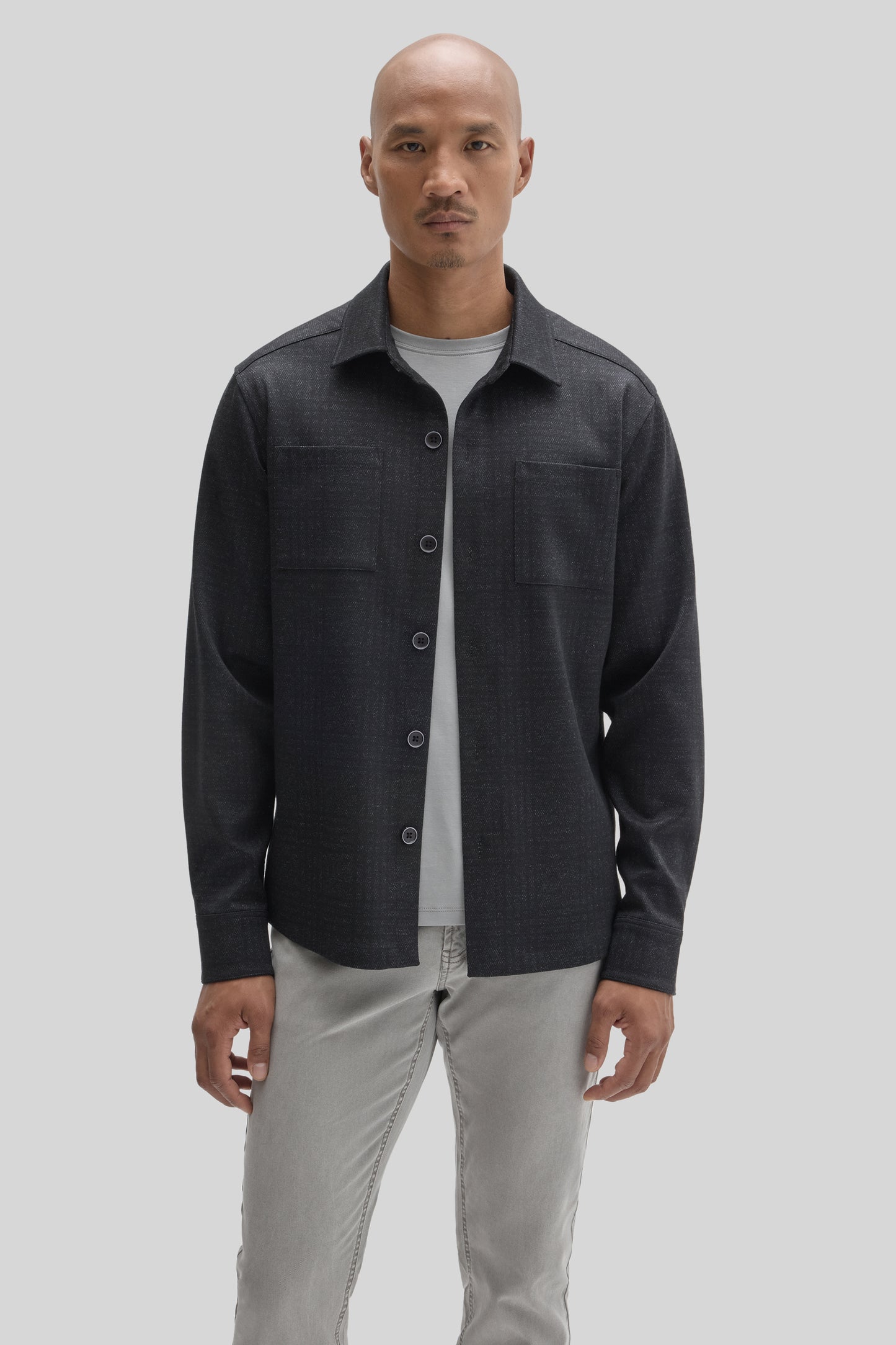Man wearing charcoal overshirt with button front and chest pockets over light gray t-shirt and beige pants.