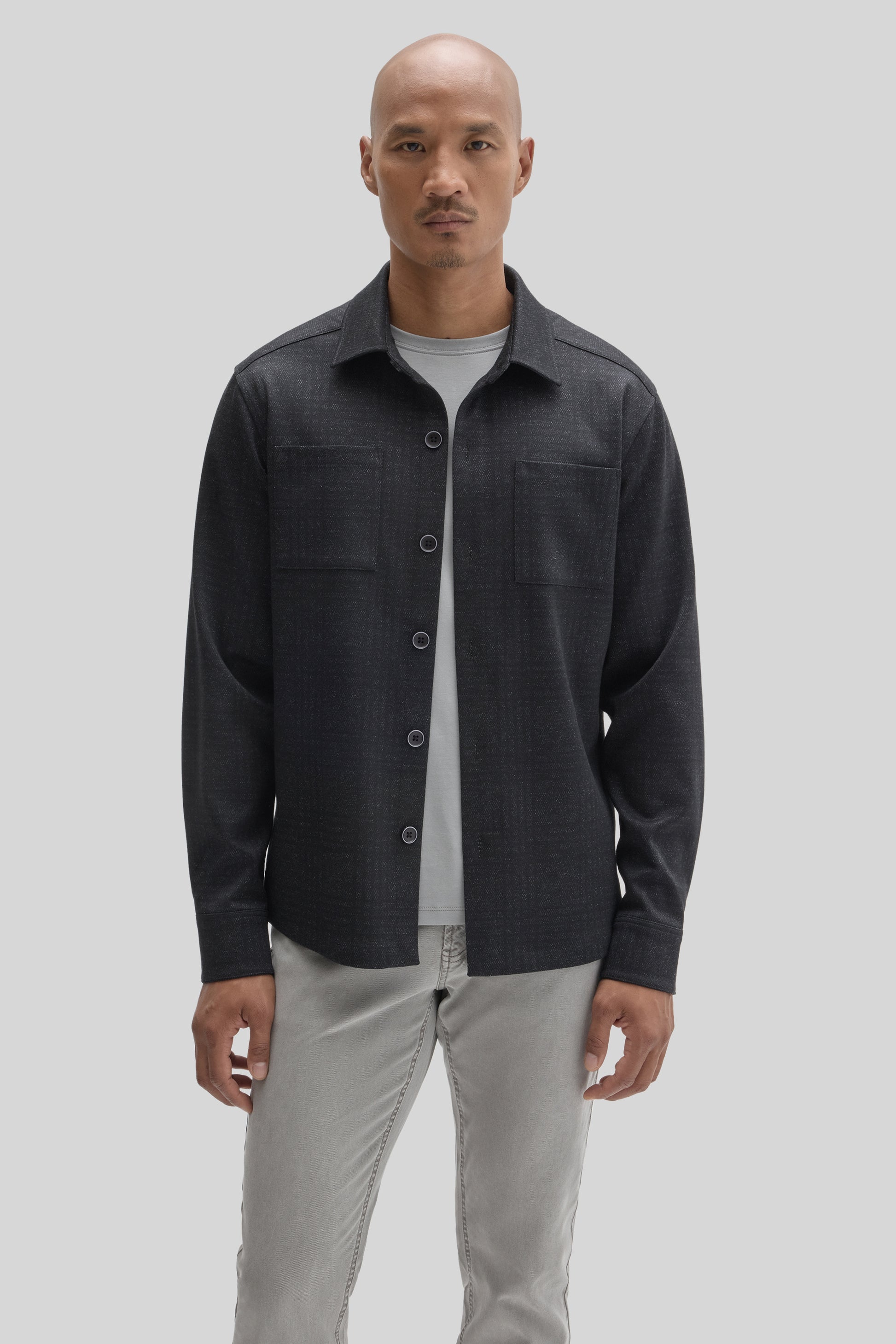 Man wearing charcoal overshirt with button front and chest pockets over light gray t-shirt and beige pants.
