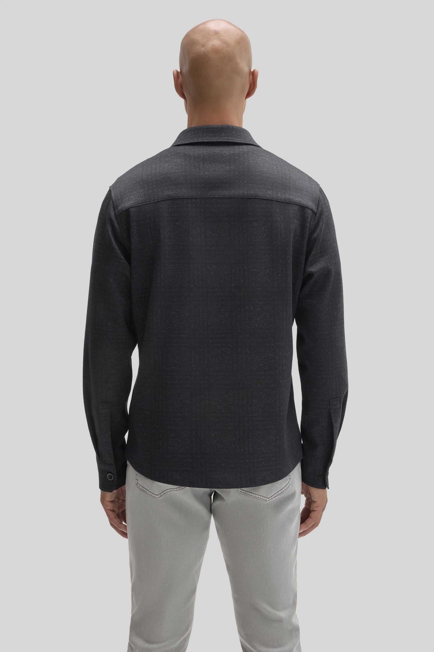 Man wearing charcoal overshirt with collar and long sleeves over beige pants, shown from back.