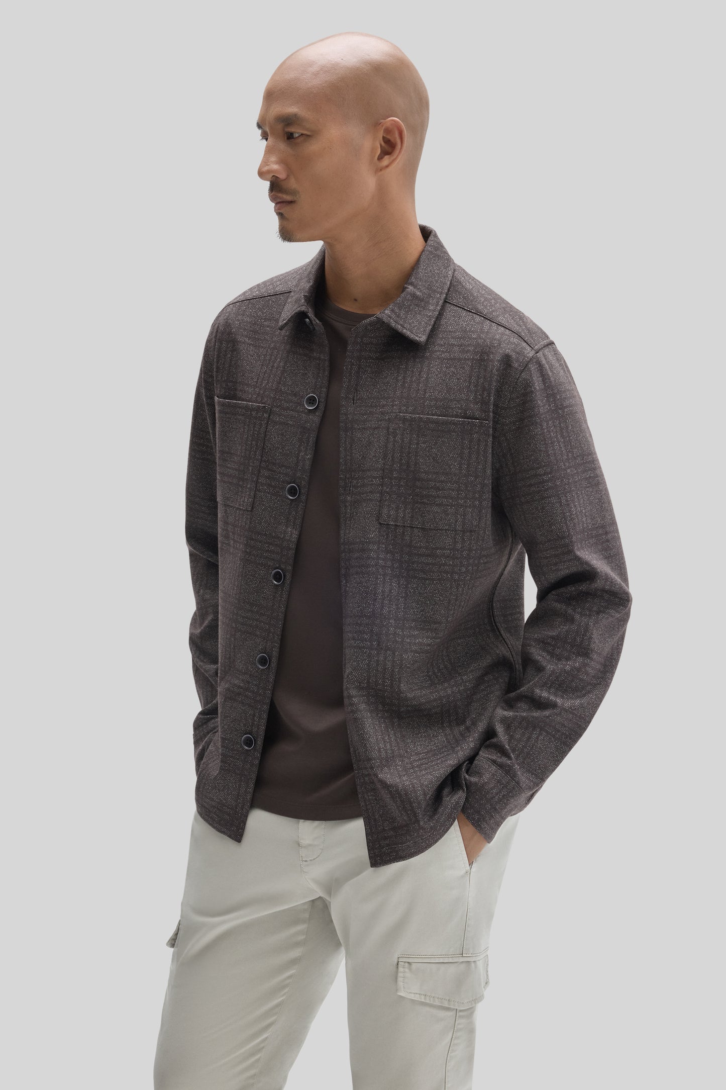 Charcoal overshirt with button front, chest pockets, and pointed collar worn over dark shirt and cream cargo pants.