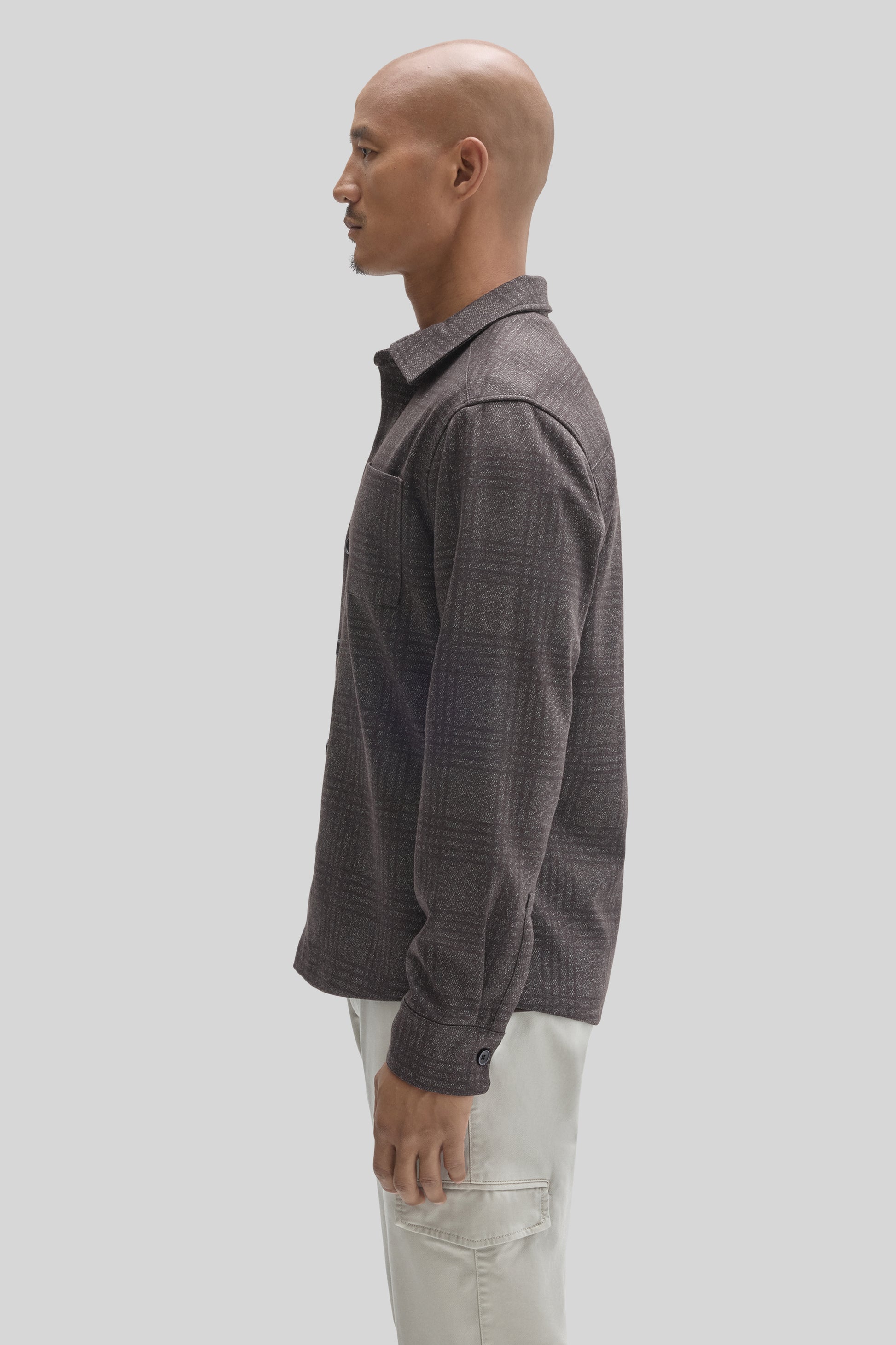 Charcoal gray overshirt with collar and long sleeves worn with cream-colored pants, shown in profile view.