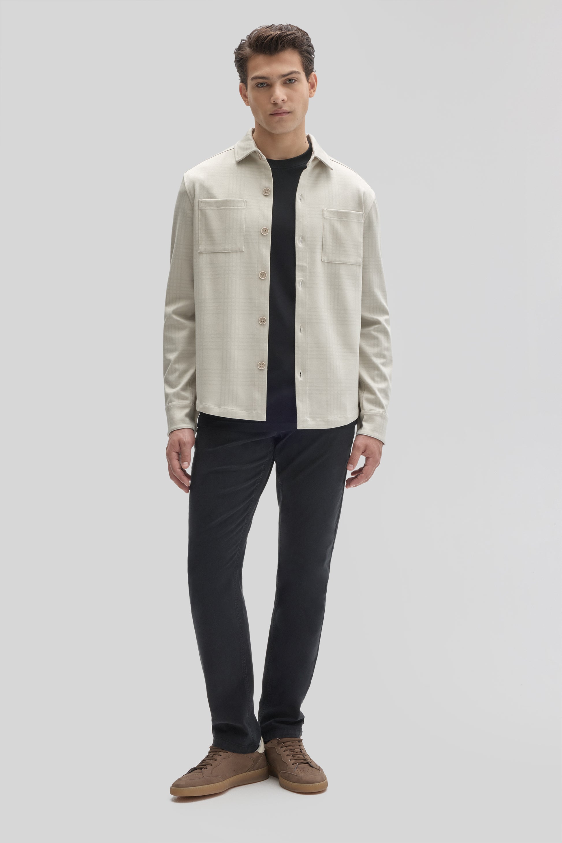 Man wearing cream overshirt with chest pockets and button front over black shirt and dark pants.