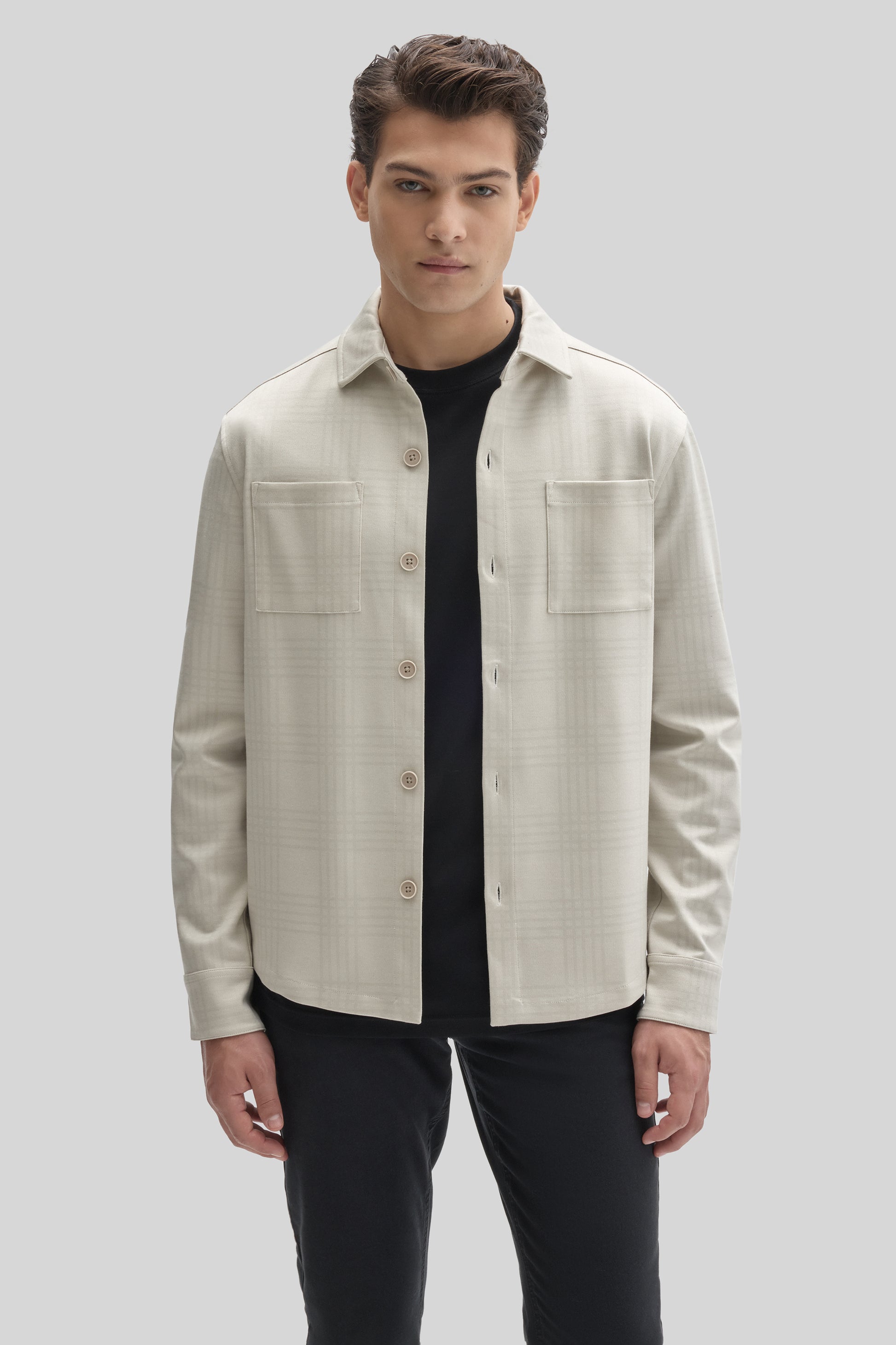 Cream overshirt with button front, chest pockets, and long sleeves worn over a black t-shirt.