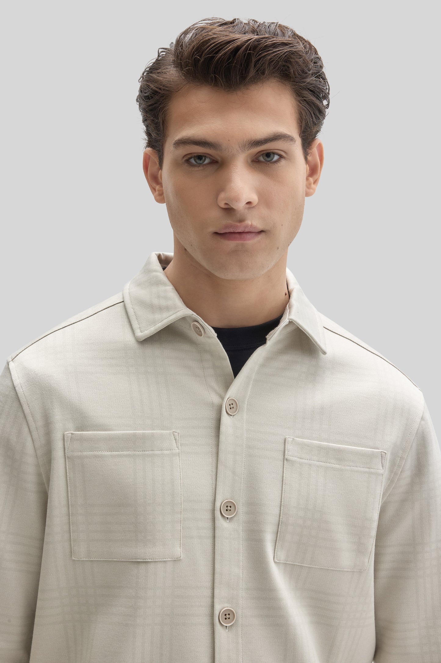 Man wearing cream-colored Upton overshirt with collar, button front, and chest pockets over black shirt.