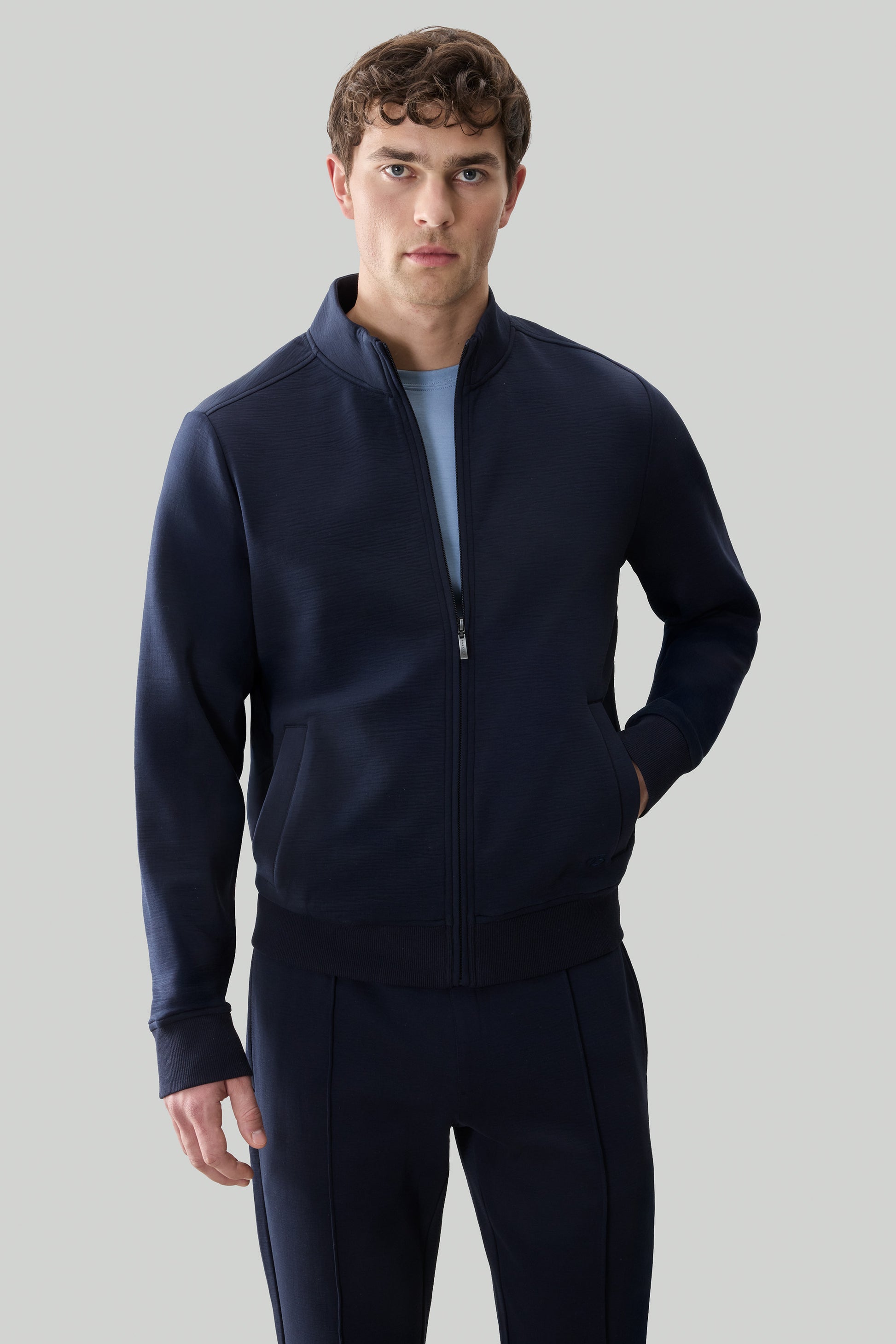 Navy long sleeve full zip jacket with textured fabric and front pockets worn over light blue shirt.