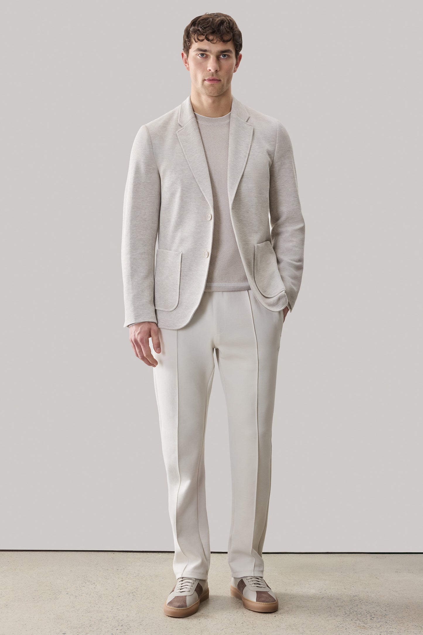 Man wearing light gray single-breasted sportcoat with notch lapels over textured knit sweater and cream trousers.